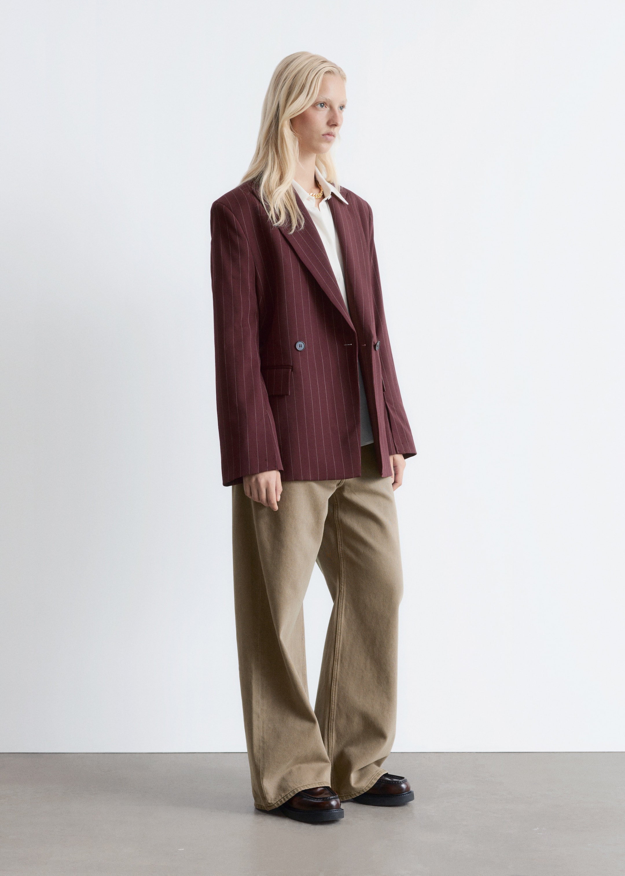Grotere afbeelding bekijken: Een bordeauxrode krijtstreep double-breasted blazer, met een dubbele rij donkere knopen, piek revers, gestructureerde schouders en voorflapzakken, wordt open gedragen door het model. Het wordt gelaagd over een wit overhemd en gecombineerd met wijde kaki broek.