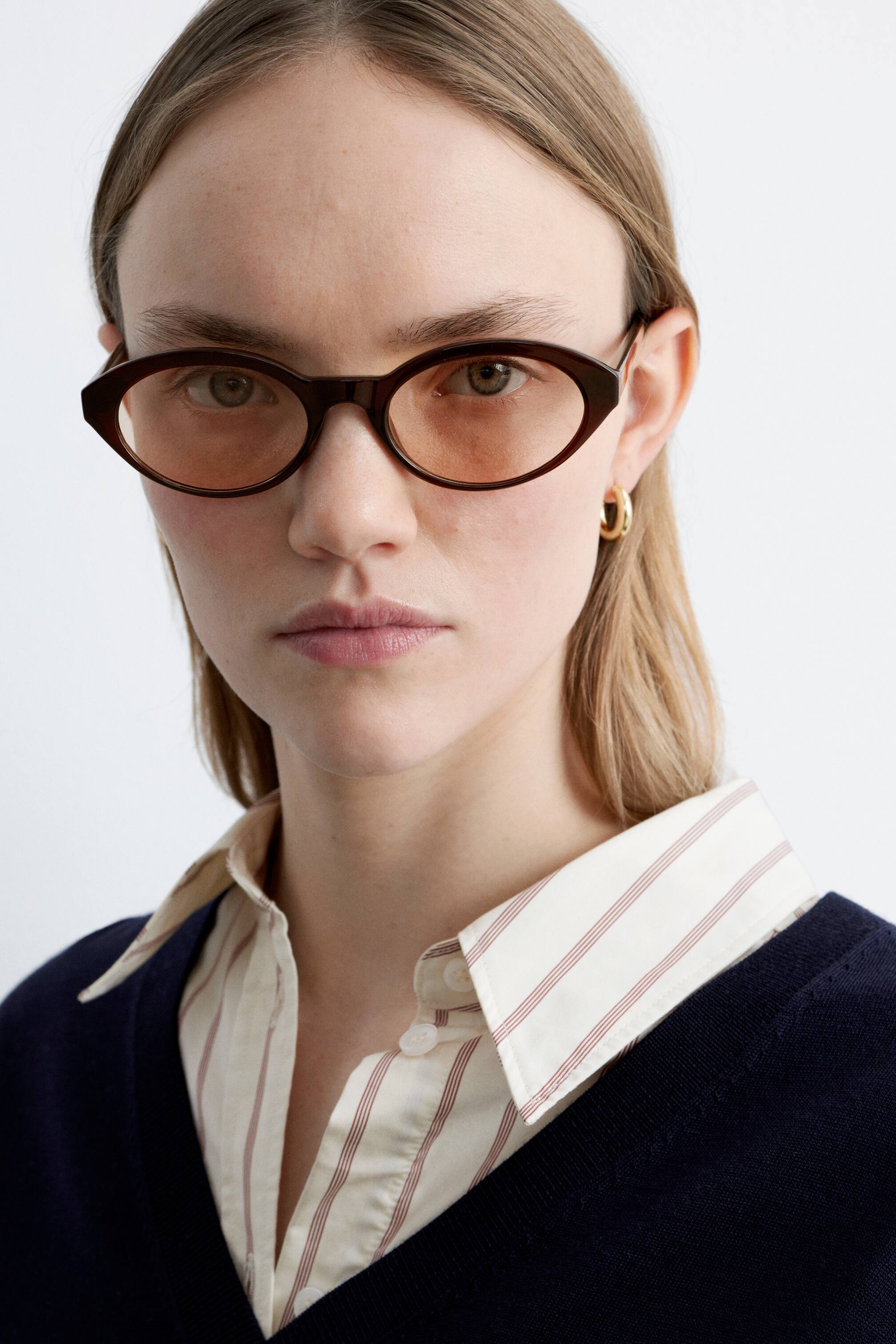 View larger image: Dark brown eyewear featuring elongated oval frames with subtle pointed outer corners, fitted with light brown tinted lenses. The eyewear is positioned facing forward on a face.
