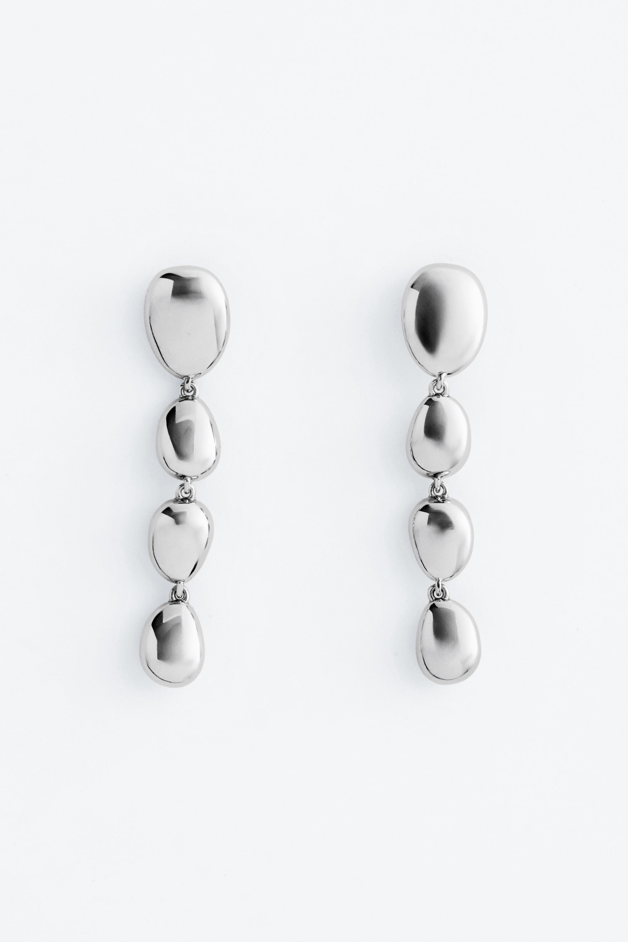 Agrandir l'image: Une paire de boucles d'oreilles pendantes ton argent est présentée de face, chacune ornée de quatre perles polies, doucement arrondies, reliées ensemble dans une chute verticale.