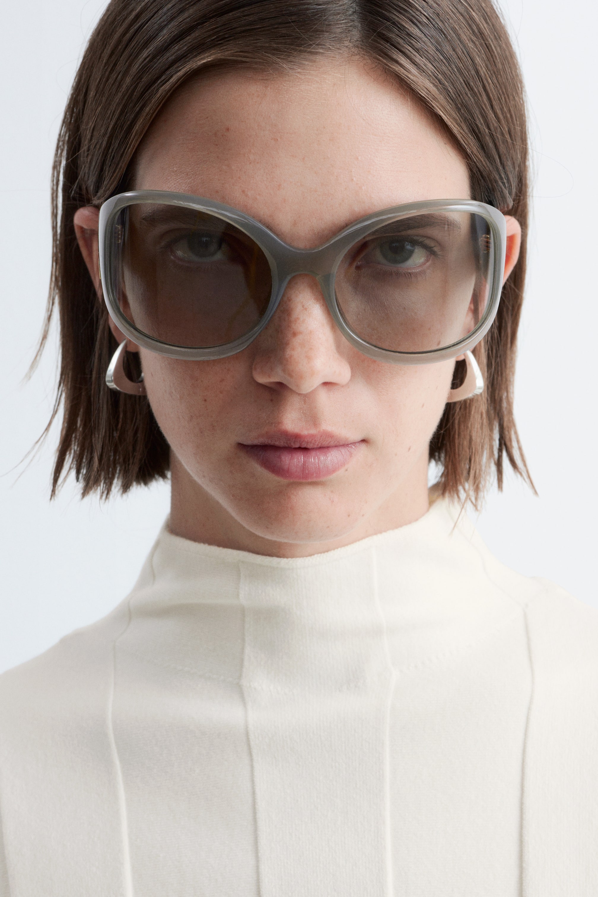 Ver imagen más grande: Se presentan unas gafas de sol grises de gran tamaño, con lentes tintadas oscuras dentro de monturas gruesas en forma de mariposa. Las monturas se ensanchan sutilmente en las sienes, demostrando su ajuste en el rostro.