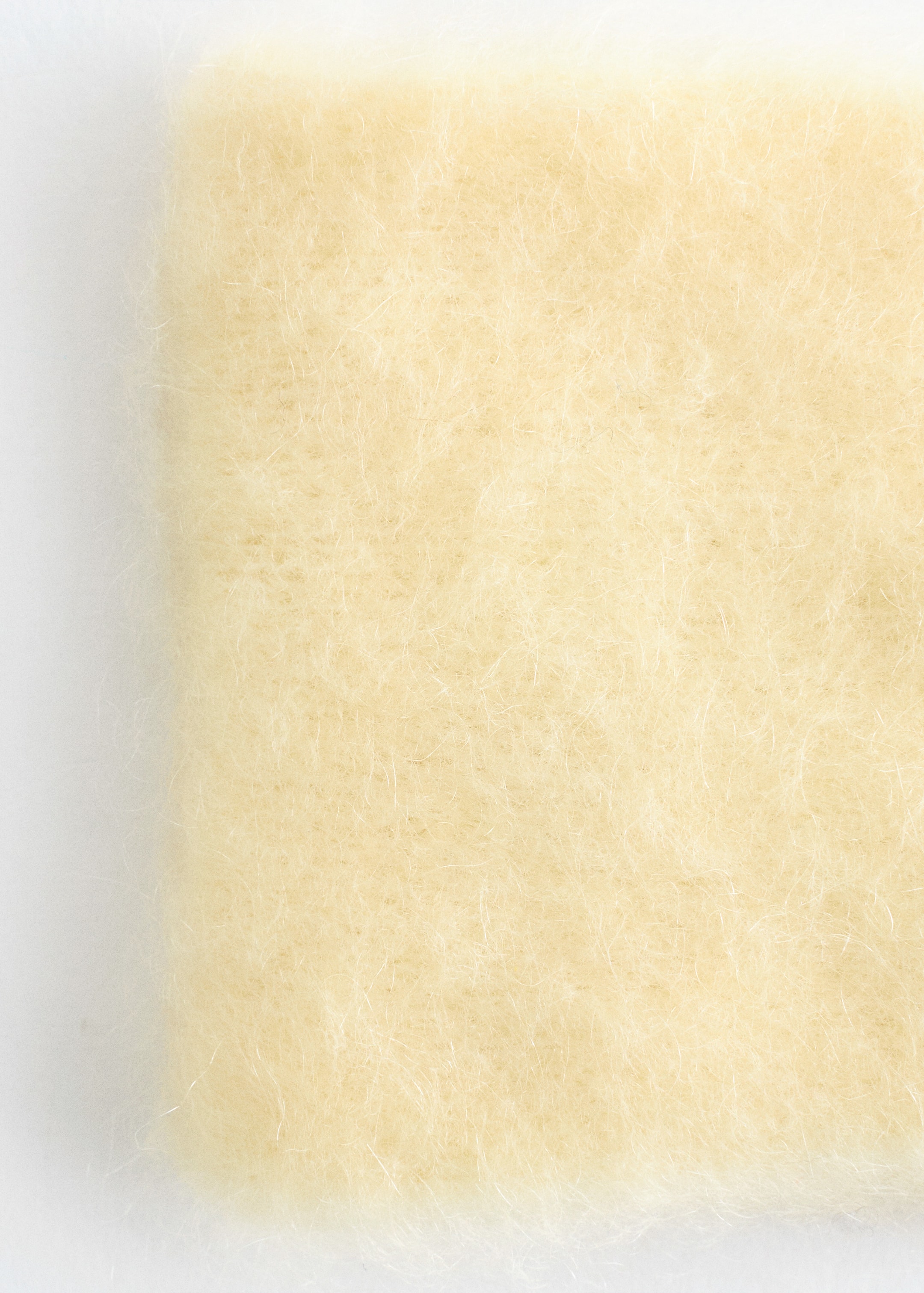Grösseres Bild ansehen: Das Mohair-Mischgewebe-Stirnband mit Twist-Front zeigt sein Material in einer Nahaufnahme und präsentiert dabei einen weichen, hellgelben Stoff mit sichtbaren, langen, feinen Fasern, die eine flauschige, strukturierte Oberfläche schaffen.