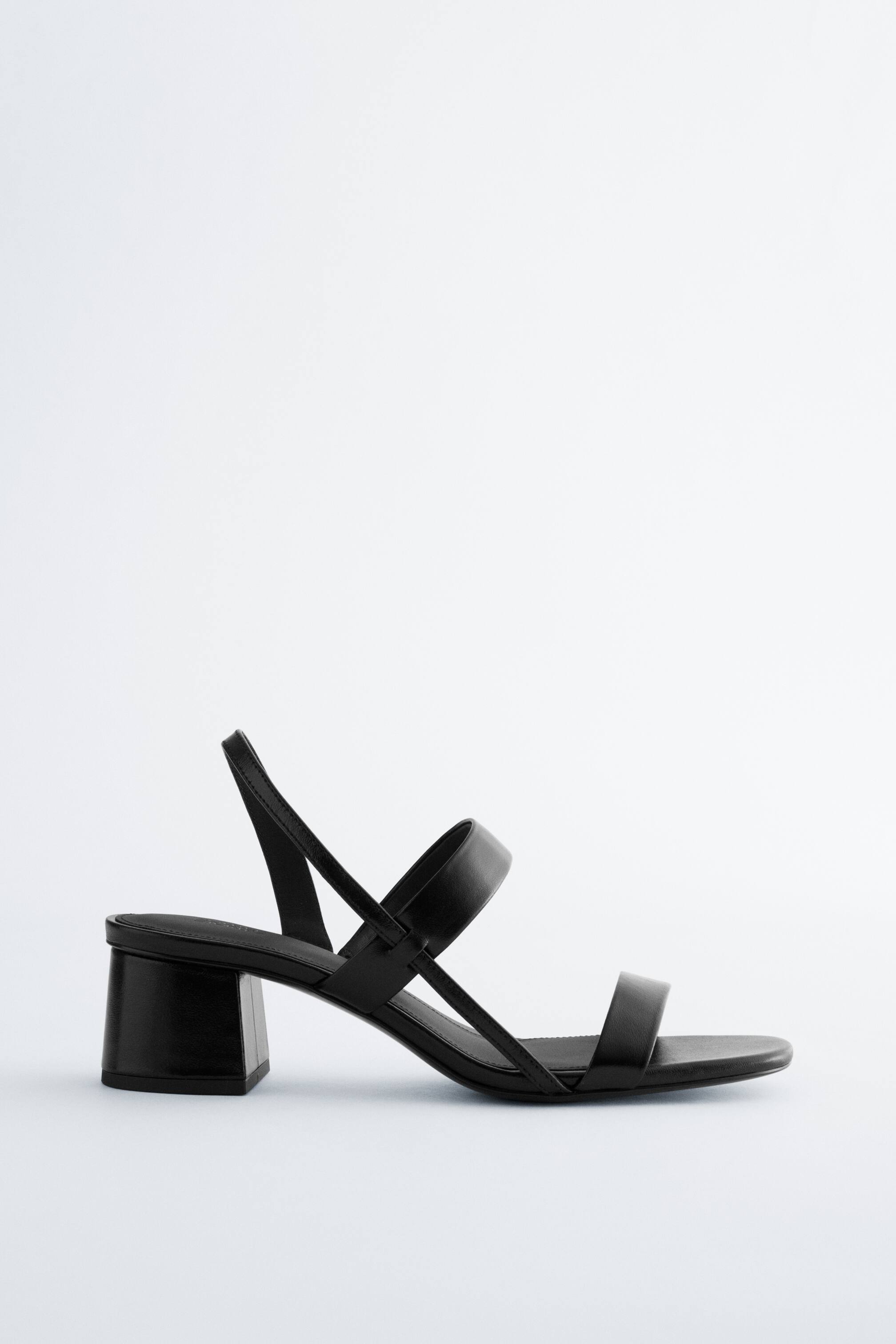 Nagyobb kép megtekintése: Egy fekete szandál, amely blokk sarkú és minimalista pántos kialakítású, két pánt keresztezi a lábfej elülső részét, és egy vékony pánt öleli körbe a sarkat, oldalnézetből bemutatva.