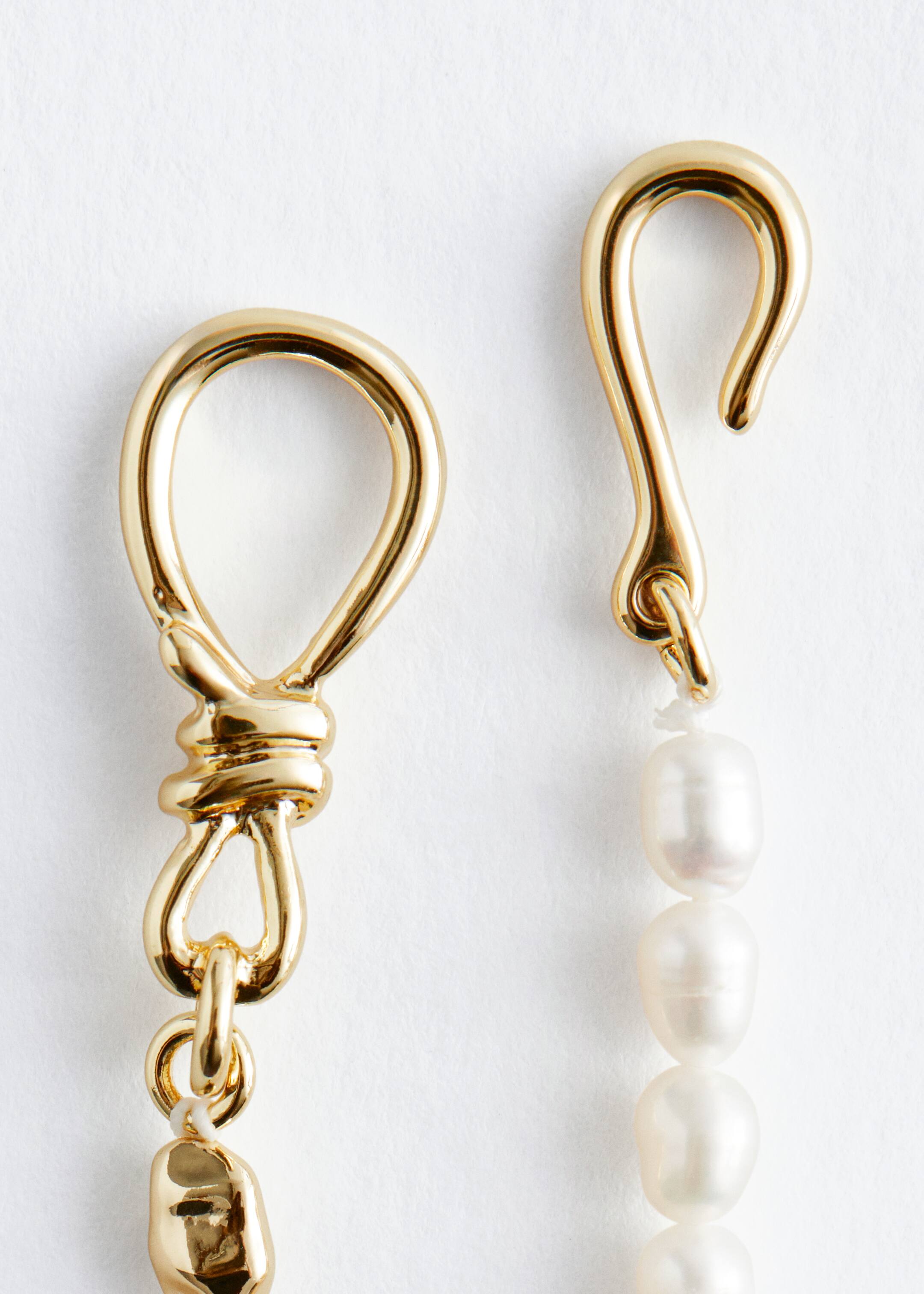View larger image: A necklace clasp is featuring a gold-toned wavy hook connecting to a strand of irregular white freshwater pearls on the right. On the left, a gold-toned knotted loop is extending from a strand with an irregular gold-toned bead, forming the two-part design.