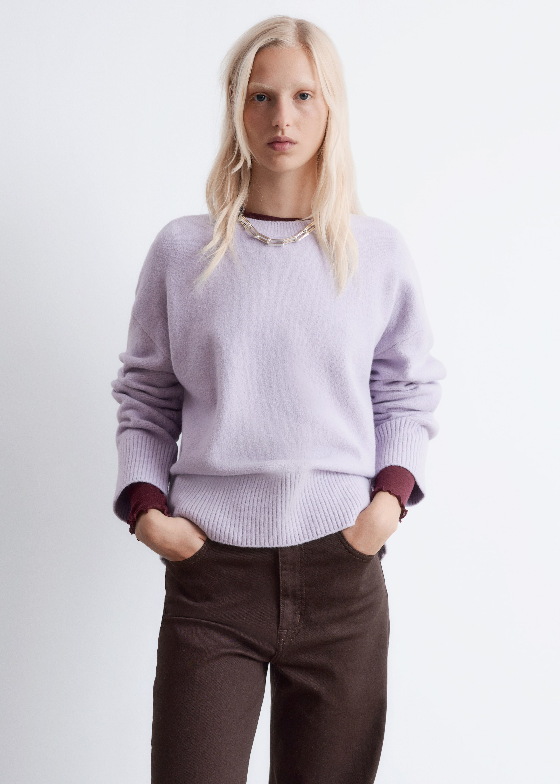 View larger image: A light purple crew-neck sweater is facing forward, featuring a soft, slightly fuzzy texture, a relaxed fit, dropped shoulders, and ribbed cuffs and hem. A dark red long-sleeved top is layering underneath, visible at the neckline and extending past the sweater's cuffs, and a silver-toned chain necklace is resting on the sweater's front.