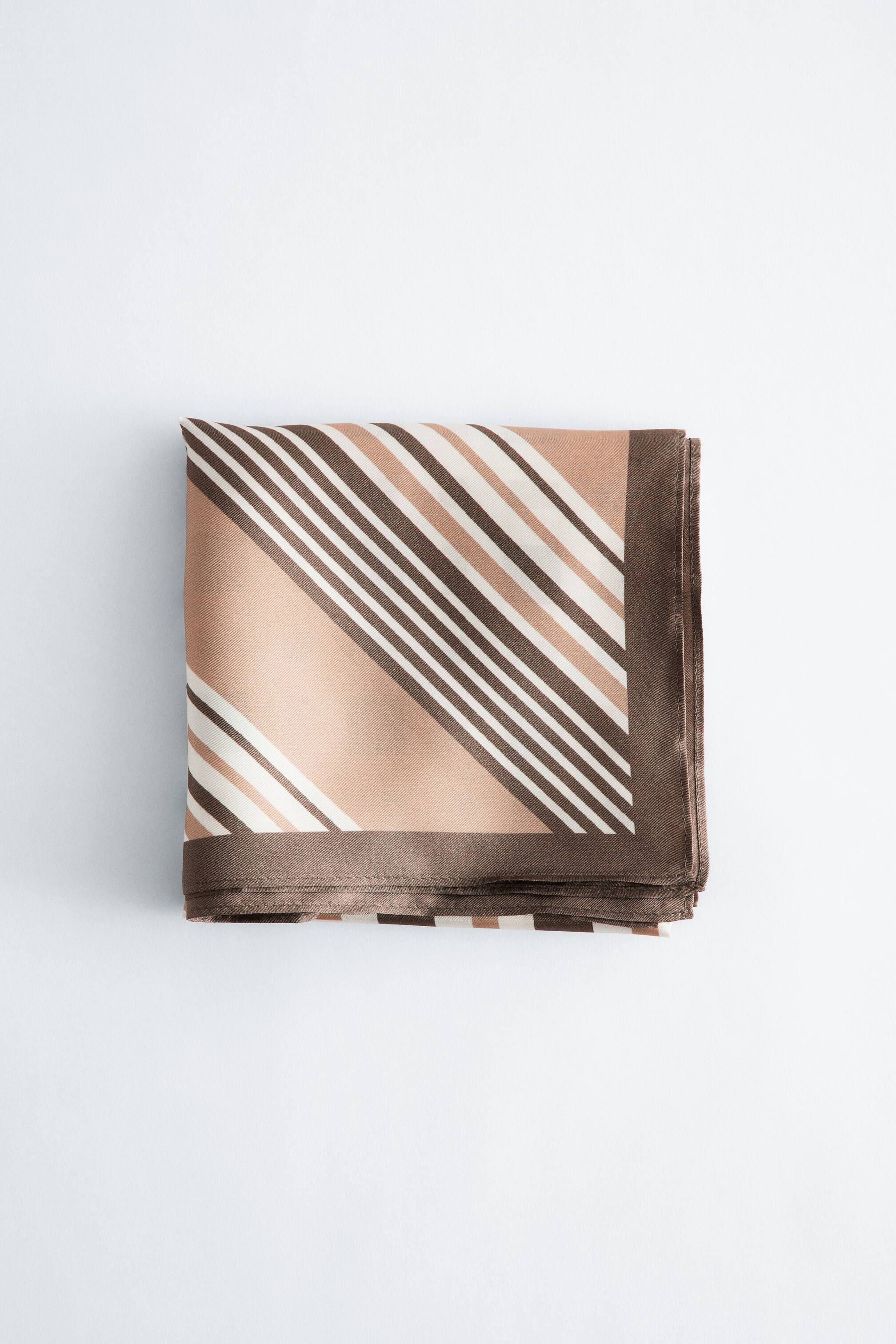 Ingrandisci l'immagine: Un foulard quadrato è piegato, mostrando un motivo con sezioni alternate a tinta unita in marrone chiaro e righe diagonali in marrone scuro e bianco, incorniciato da un bordo a tinta unita marrone scuro.