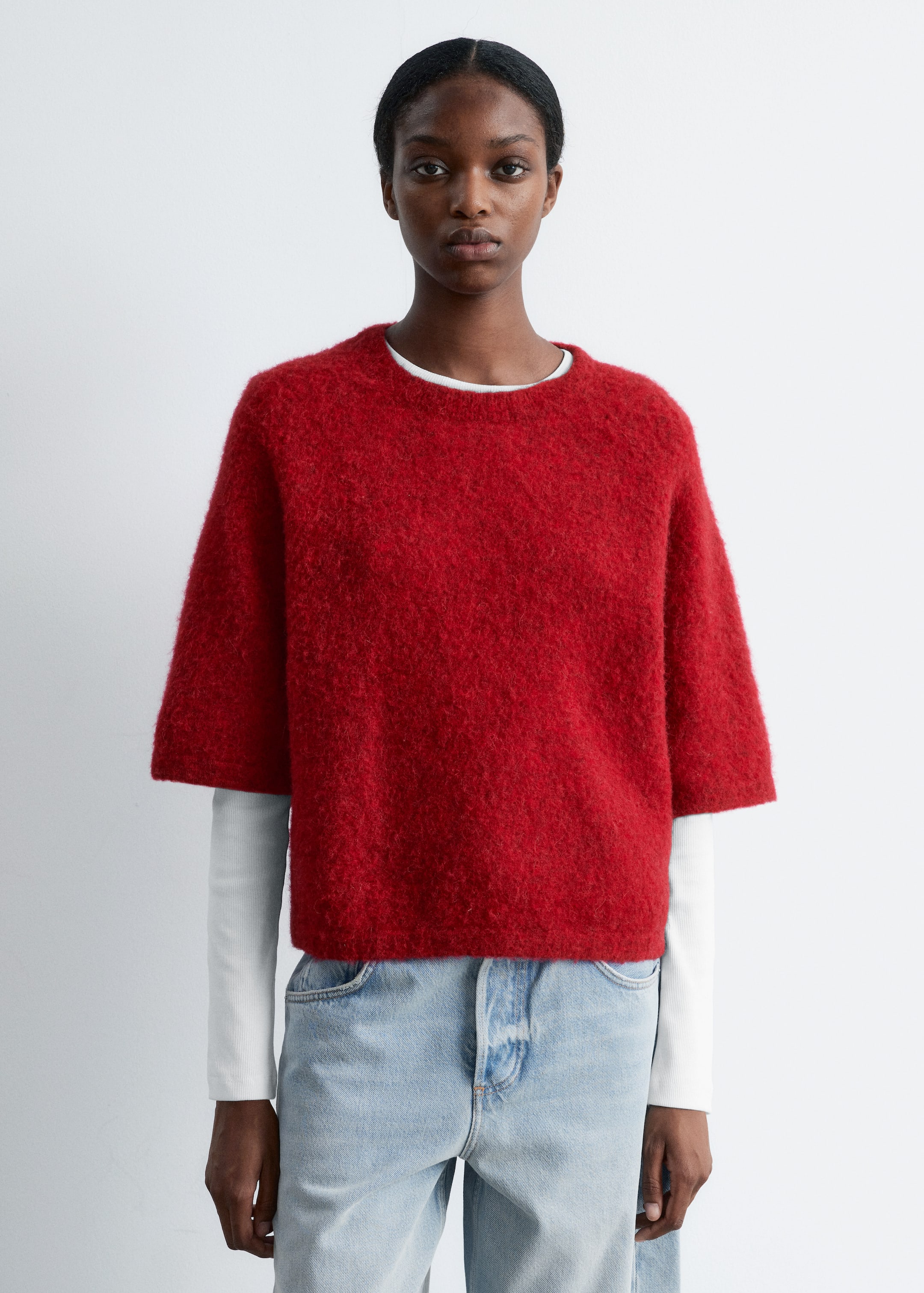 Grösseres Bild ansehen: Ein roter kurzärmeliger Pullover mit einer flauschigen, gebürsteten Textur wird über einem weißen langärmeligen Oberteil getragen. Der Pullover hat einen Rundhalsausschnitt und eine kastige, kurze Passform.