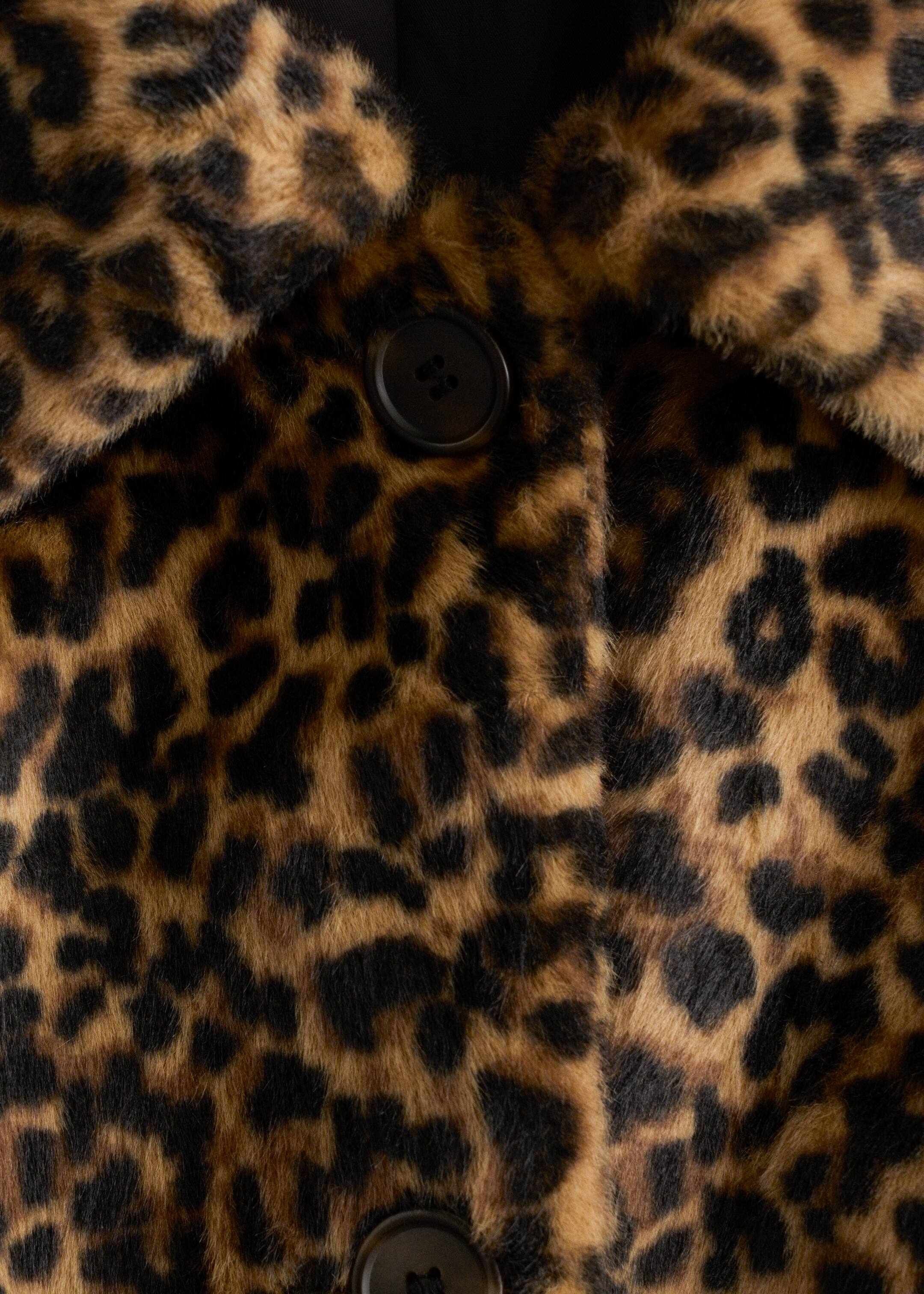 Se større billede: En frontvisning af en faux fur frakke fremhæver et brunt og sort leopardprint. Frakken har en bred, blød krave og to mørke, runde knapper på dens frontlukning.