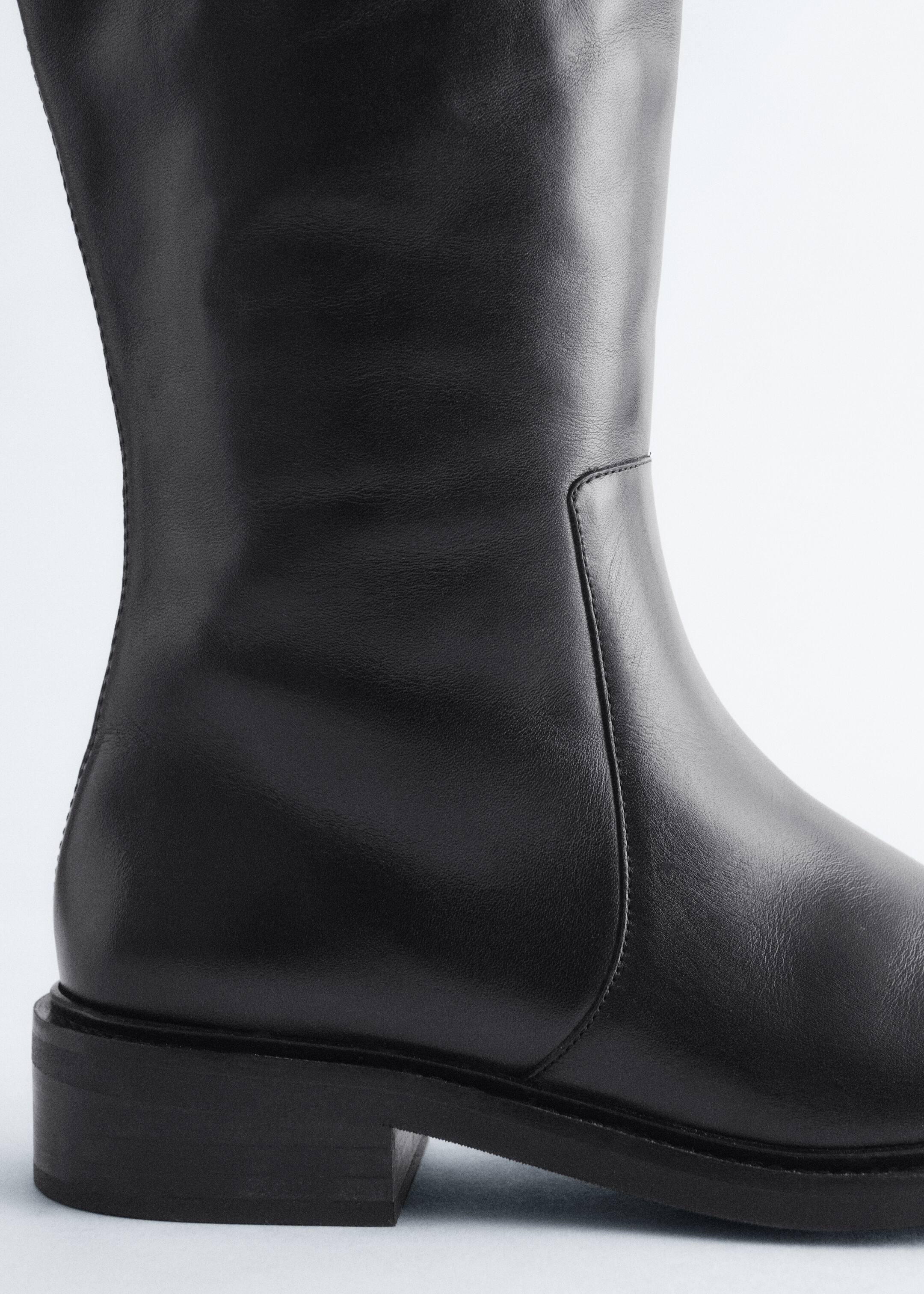 Größeres Bild anzeigen: Ein schwarzer Lederstiefel wird aus der Seitenansicht gezeigt, mit einer glatten, geschmeidigen Textur, einem niedrigen, gestapelten Blockabsatz und einer vertikalen Naht, die den Schaft hinauf verläuft. Der Stiefel ruht auf einer flachen, stabilen Sohle.