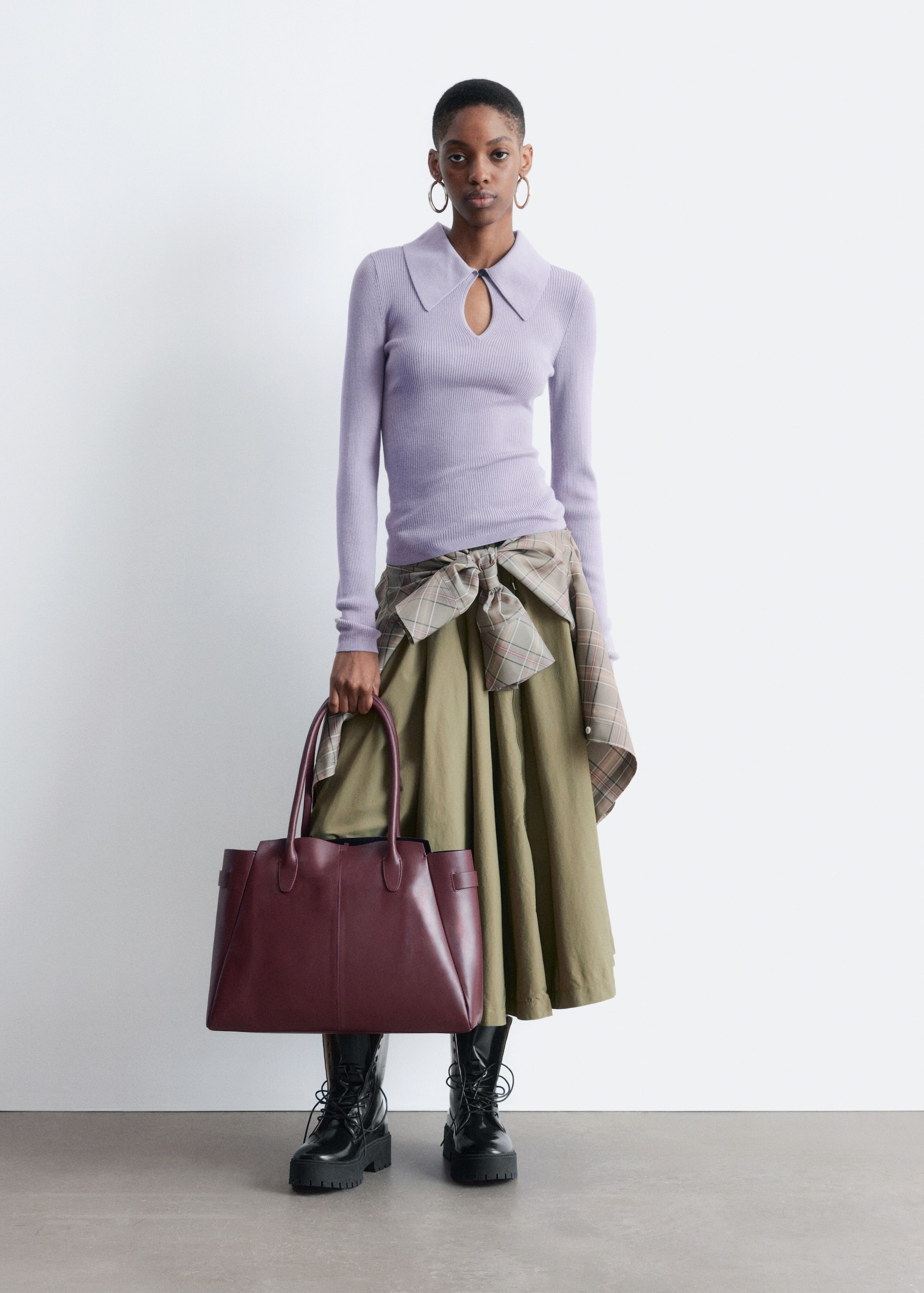 View larger image: A burgundy tote bag is being held by a hand, facing forward. It is displaying a structured shape in a smooth material, with two top handles, vertical front seams, and side strap details cinching the top.