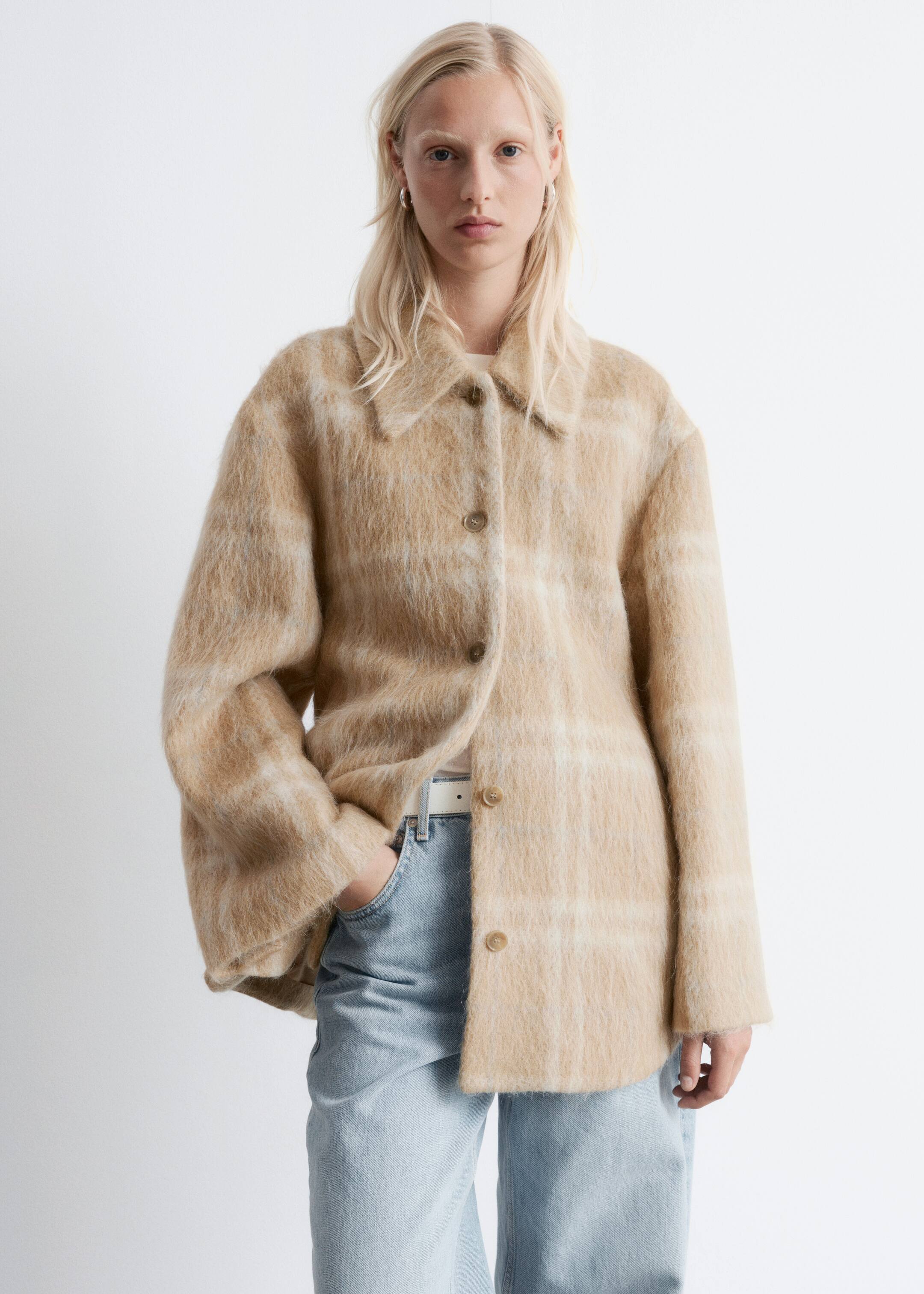 View larger image: A fuzzy, hip-length jacket in a beige and cream plaid pattern is being shown from a front-facing, slightly angled perspective. It is featuring a pointed collar and a front button closure with round, light brown buttons.