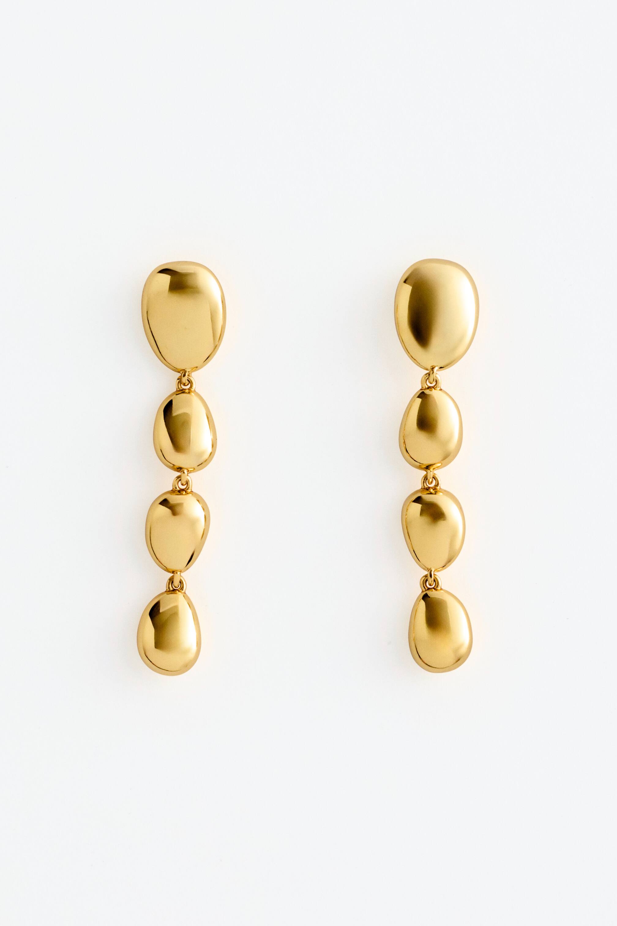 View larger image: A pair of polished brass pendant earrings is shown from the front, featuring four softly rounded beads vertically descending.