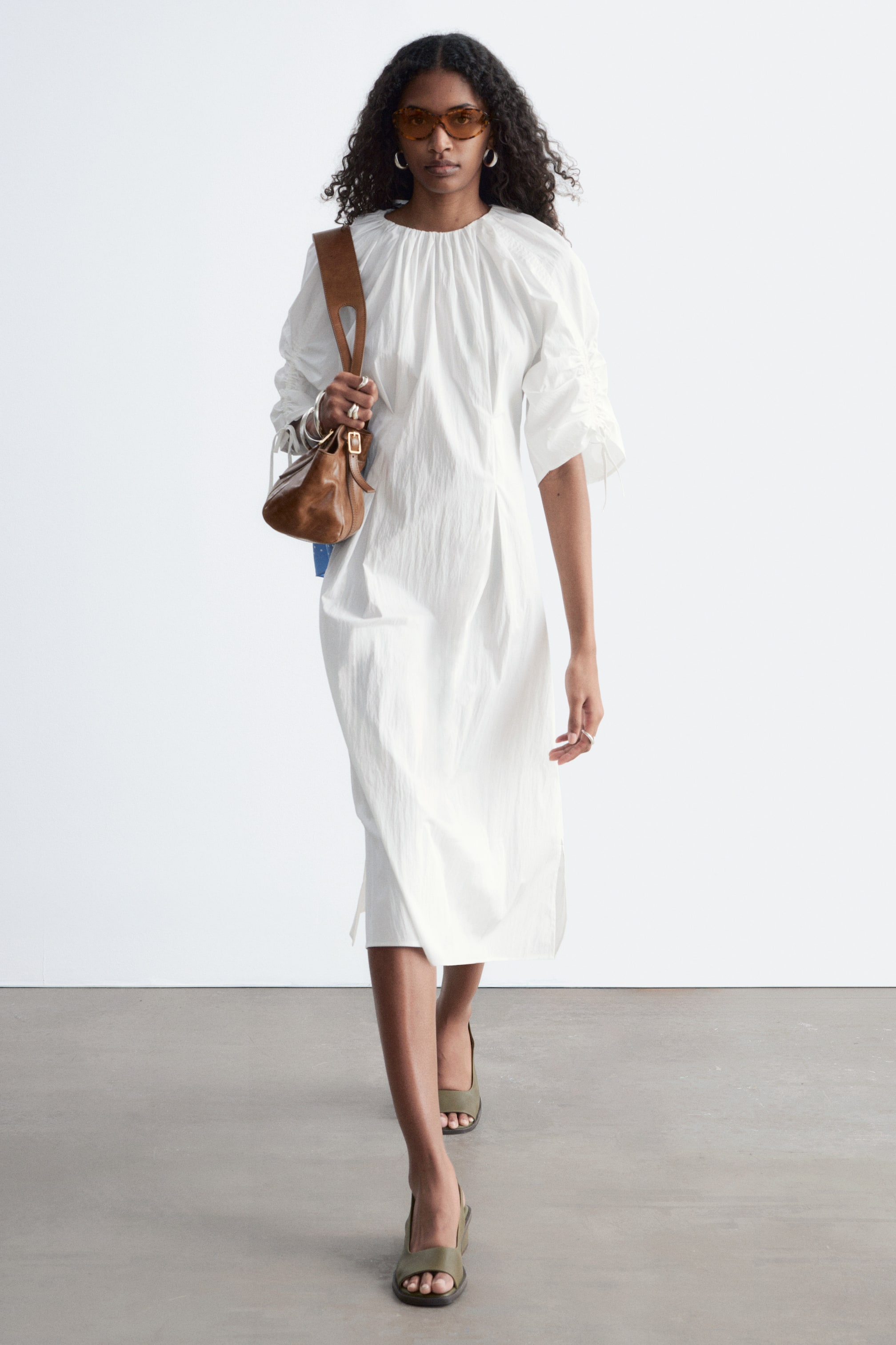Visualizza immagine più grande: Un abito midi bianco presenta un girocollo arricciato e maniche a tre quarti voluminose con dettagli arricciati, presentate ad un angolo leggero. Mostra una silhouette rilassata con pieghe verticali sul corpetto e sulla gonna, e spacchi laterali sull'orlo.