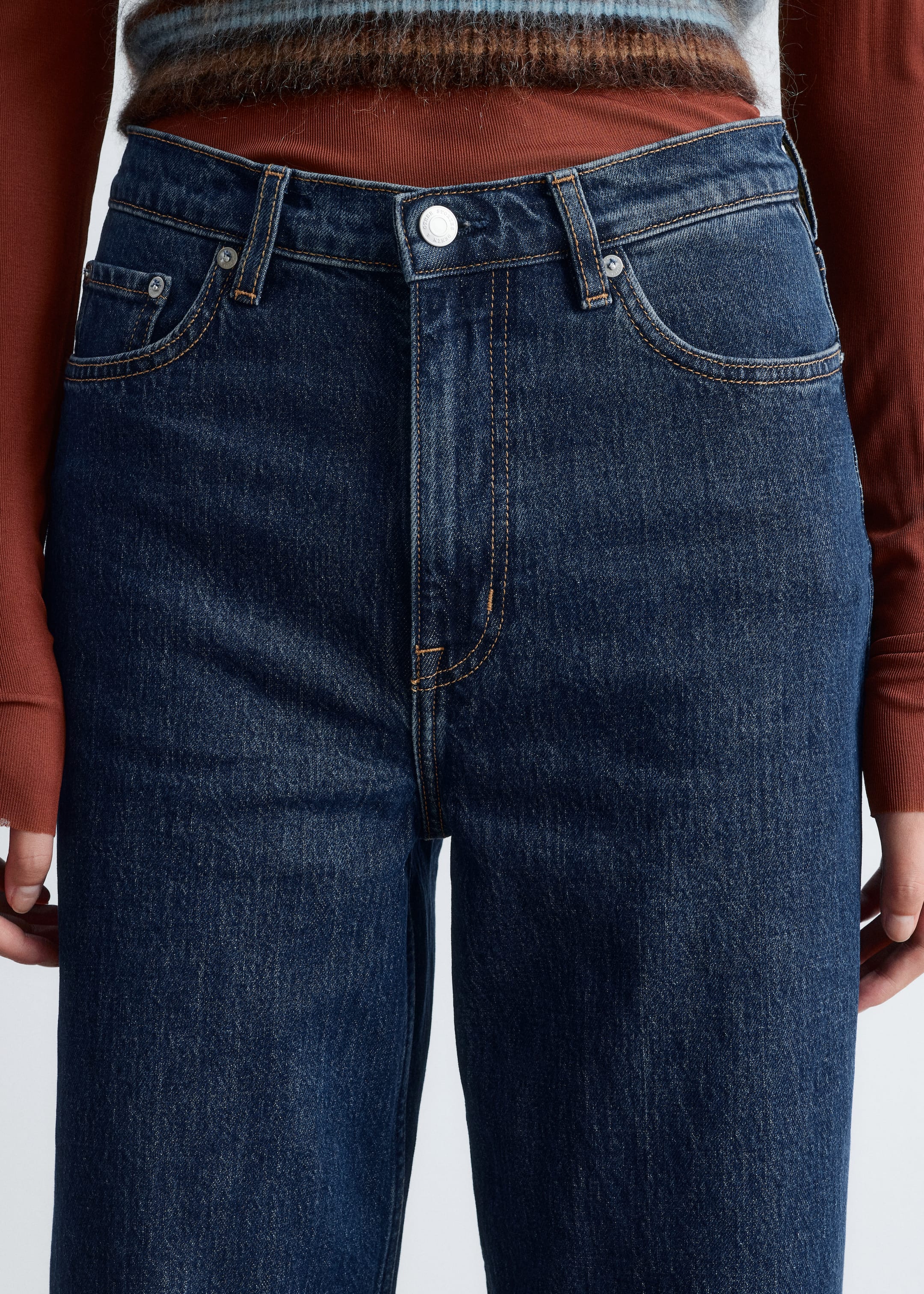 View larger image: Dark blue denim jeans are featuring a waistband with belt loops, a single silver-toned button closure, and a zipper fly. Two curved front pockets and a coin pocket are visible, accented with silver-toned rivets and light brown contrast stitching, as the jeans are being shown from a front, close-up angle.
