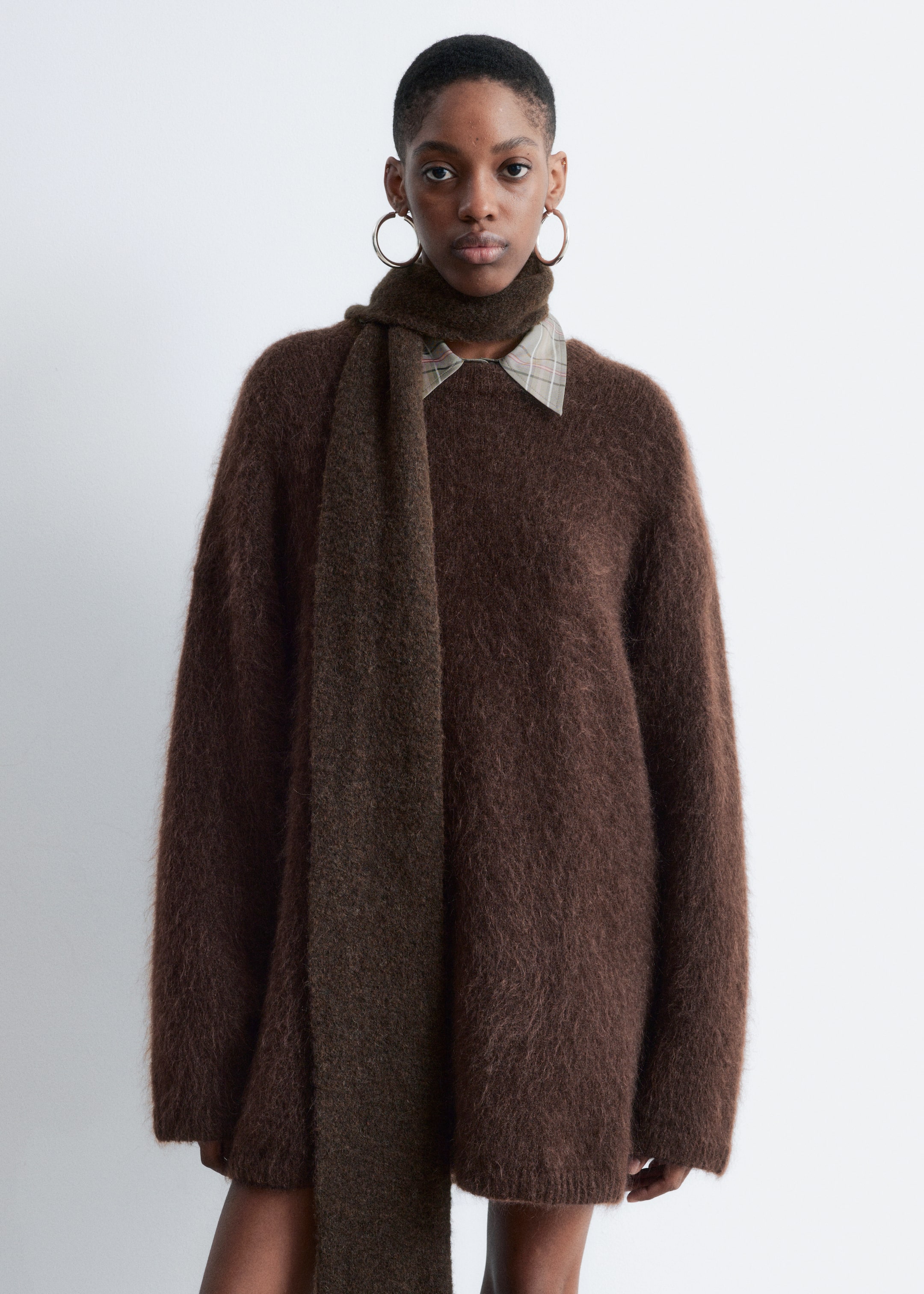 View larger image: A long, oversized, fuzzy brown sweater is being shown from the front. It is layered over a light-colored plaid shirt, with the collar visible at the neckline, and a dark brown fuzzy scarf is draped around the neck, hanging down the front.