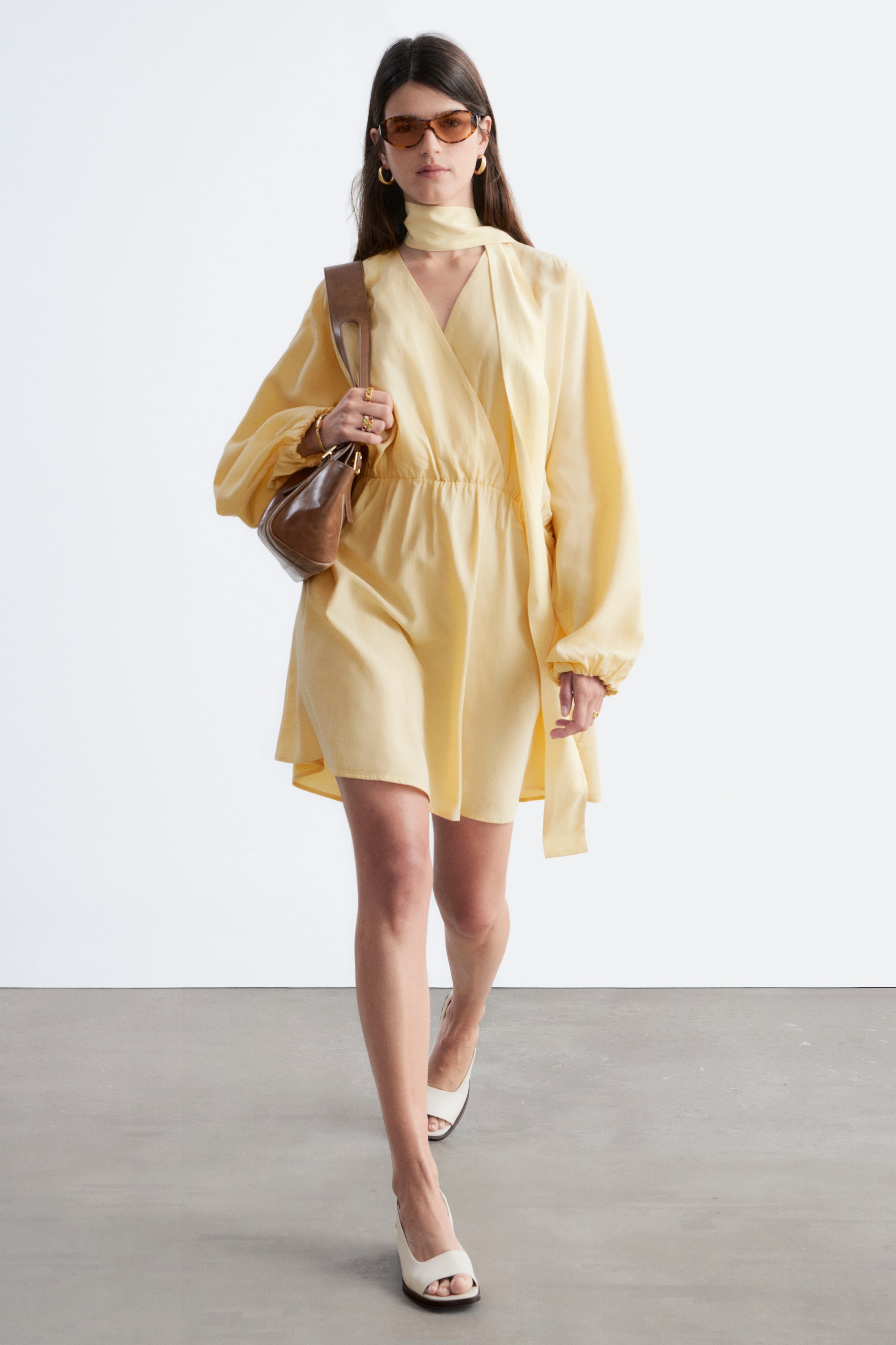 Преглед на по-голямо изображение: Светложълтата мини рокля е с V-образно деколте в стил "прегърни ме" и самозавързващ се шал, дълги обемни ръкави, събрани на маншетите, и еластична талия, която преминава в разкроена пола.