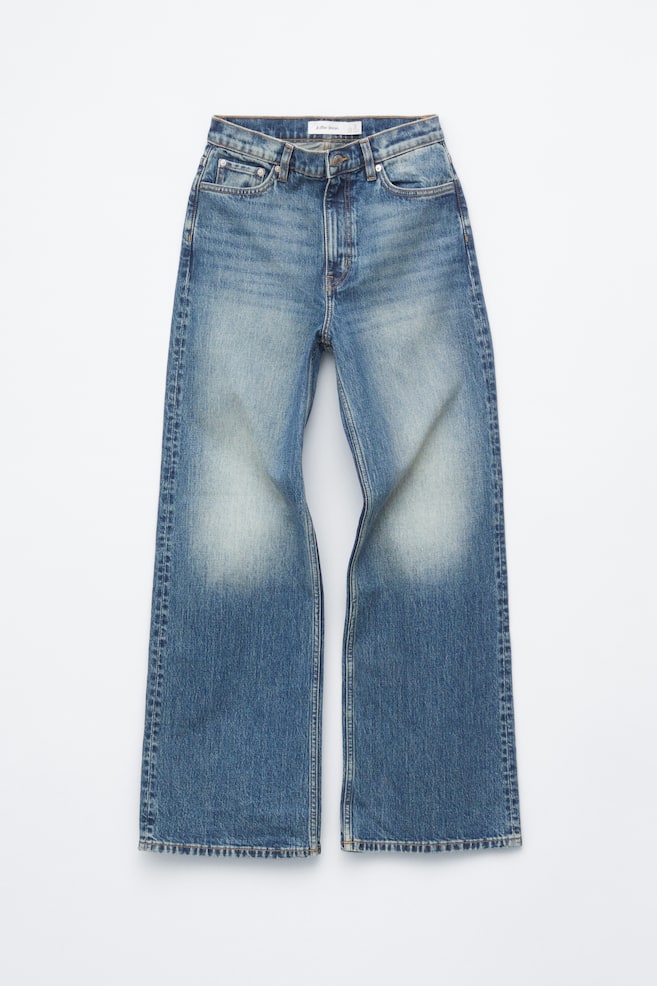 A pair of high-waisted blue denim jeans is showcasing its front view, laid flat, featuring a classic 5-pocket design, a zip and button fly, and long, wide legs. The denim exhibits a faded wash on the thighs, transitioning to a darker blue on the lower legs. - 1