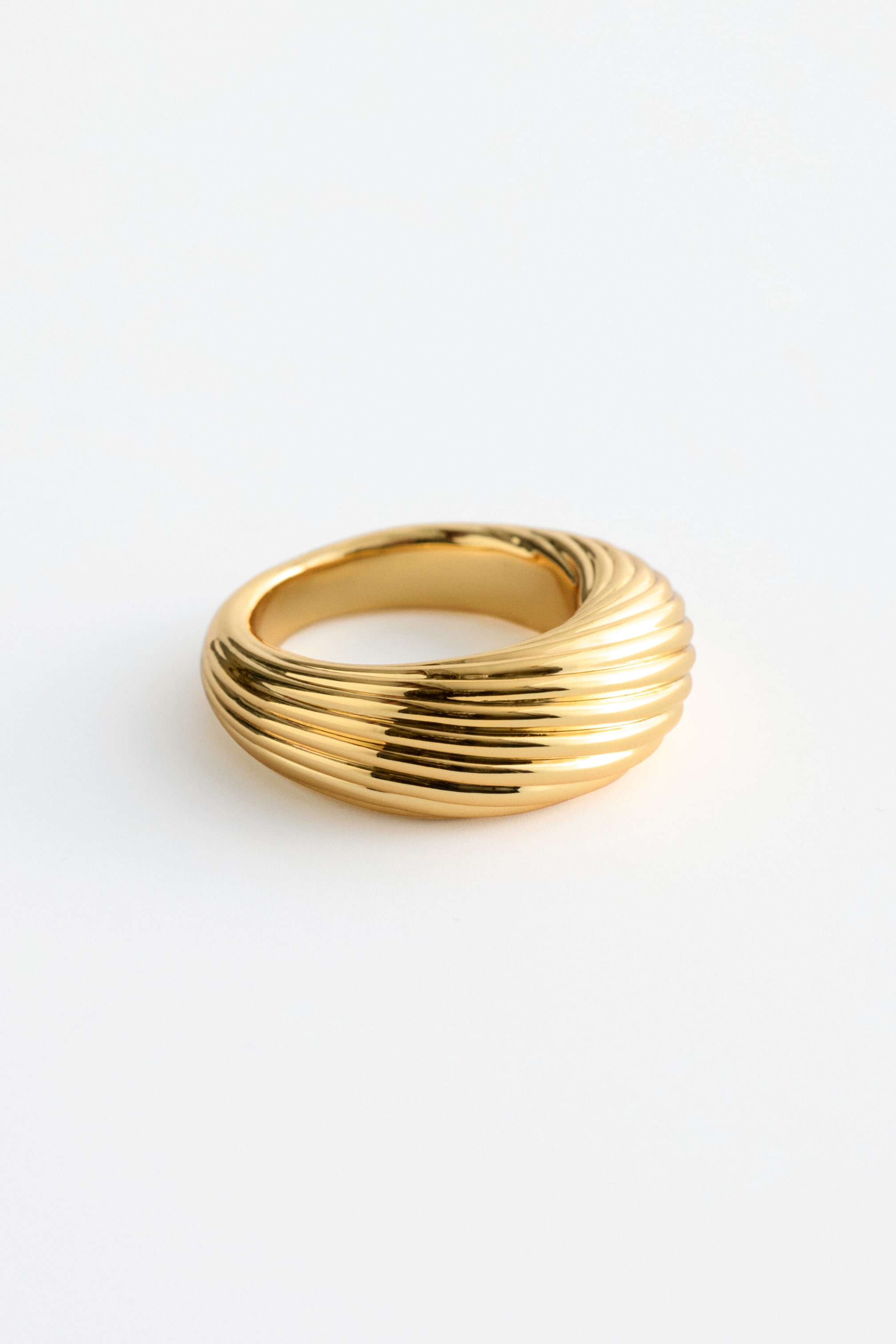Grotere afbeelding bekijken: Een goudkleurige ring met een dikke, brede band en een gegroefd textuur. De ring wordt gepresenteerd onder een lichte hoek, waarbij het gepolijste oppervlak en de parallelle groeven die rond de vorm lopen, zichtbaar worden.