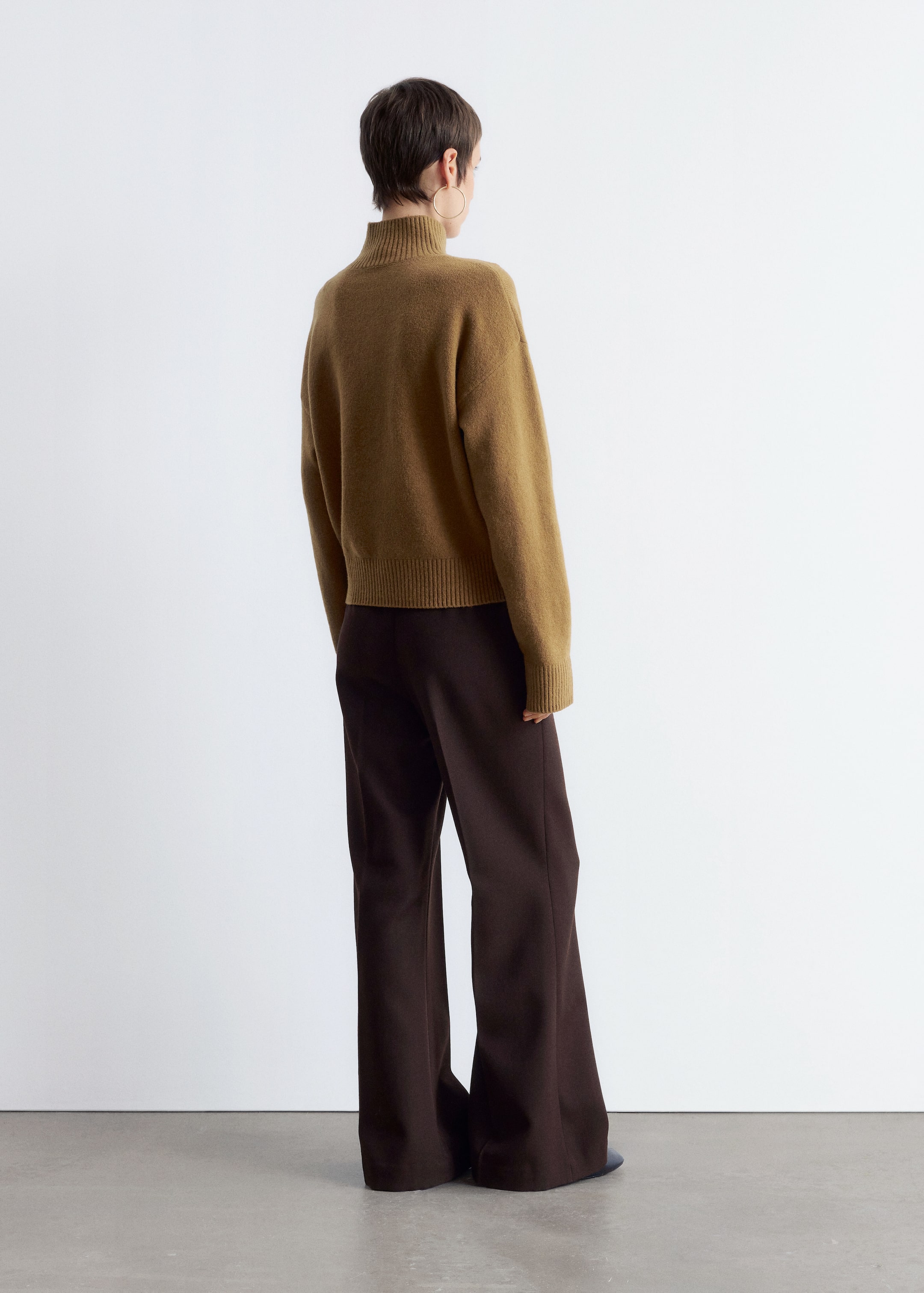 Agrandir l'image: Un pull en maille marron à coupe ample est porté par le mannequin, avec un col roulé côtelé, des épaules tombantes et des bords-côtes aux poignets et à l'ourlet. Le mannequin l'associe à un pantalon large marron foncé.