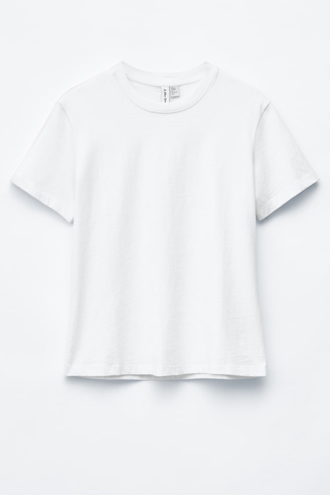 Un tricou alb este prezentat din față, având un decolteu rotund cu nervuri și mâneci scurte, afișând o siluetă dreaptă, cu o croială obișnuită. - 1
