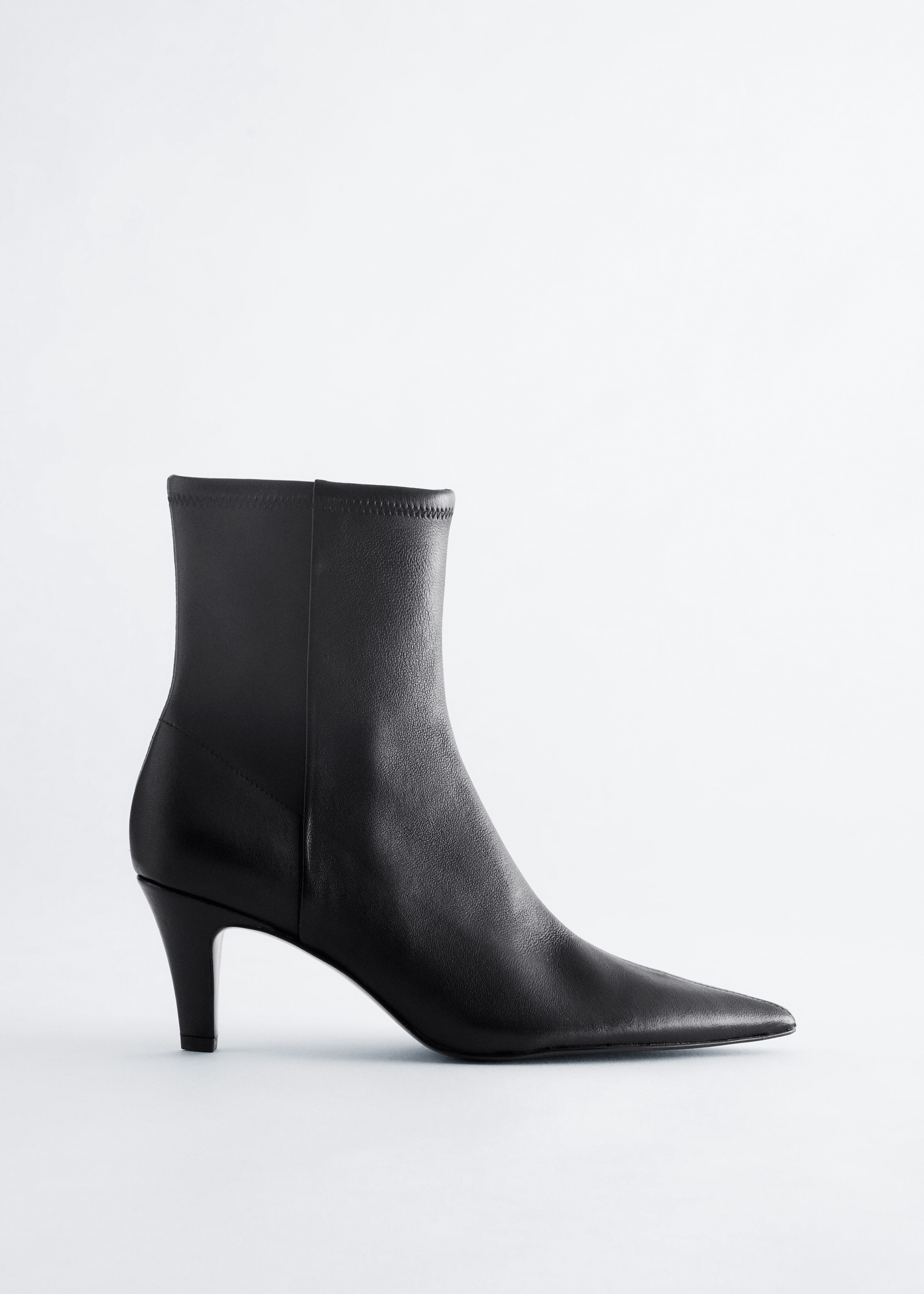 Black leather sock boots featuring a pointed toe and stiletto heel are worn by the model under wide-leg grey trousers.