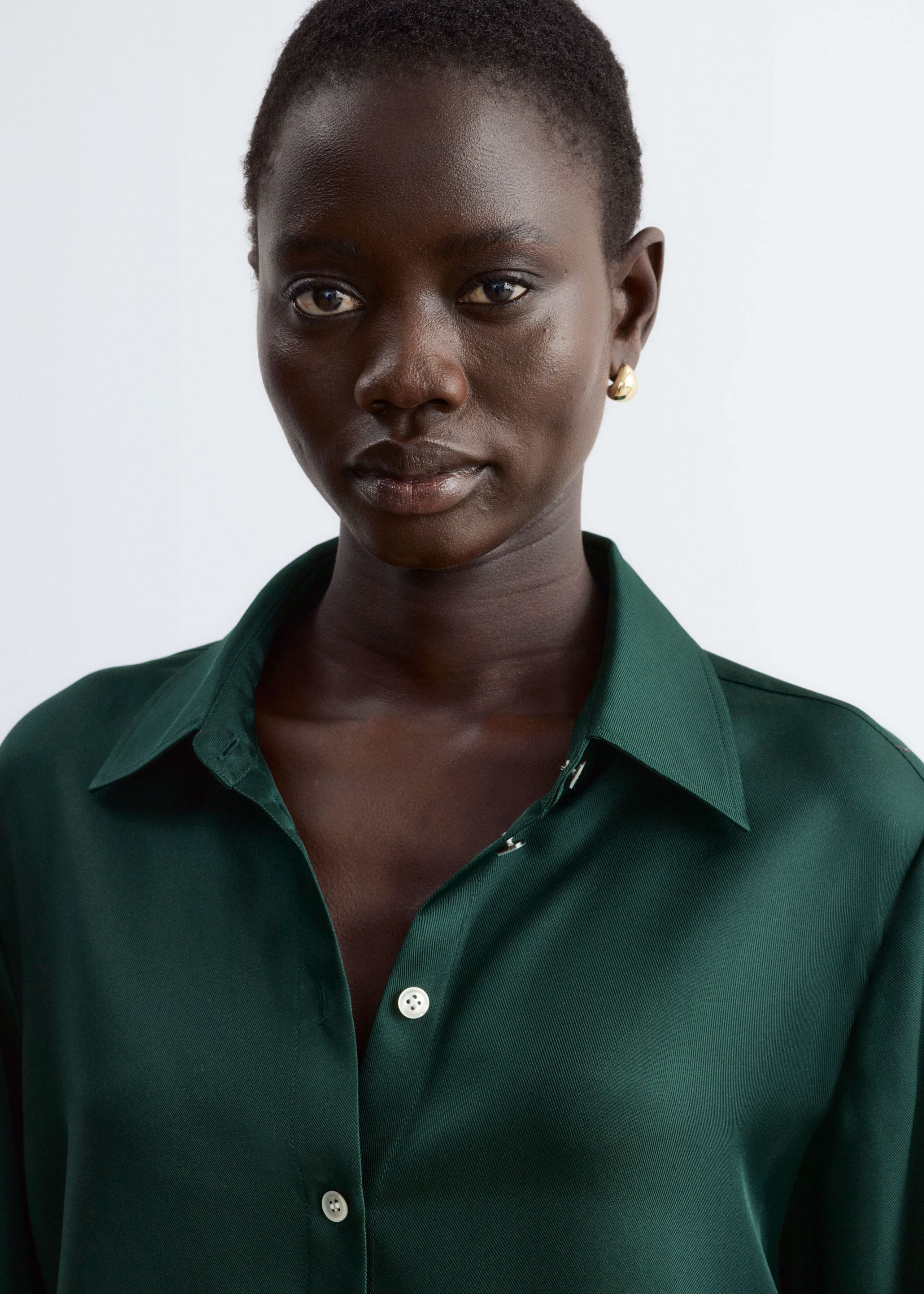 A dark green silk shirt with a subtle sheen is being worn by the model. The shirt features a classic pointed collar, left slightly open at the neck, and contrasting light-coloured buttons along the front placket.