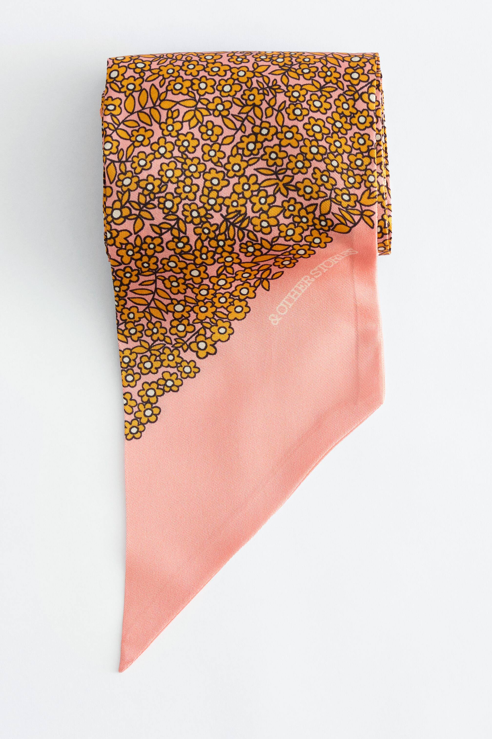Se større billede: Et slankt tørklæde med et tæt blomsterprint af små gule blomster med mørke konturer på en lyserød baggrund, der gradvist går over i en ensfarvet lyserød, tilspidset ende. Mærkenavnet "& OTHER STORIES" er diskret synligt på den ensfarvede lyserøde sektion.