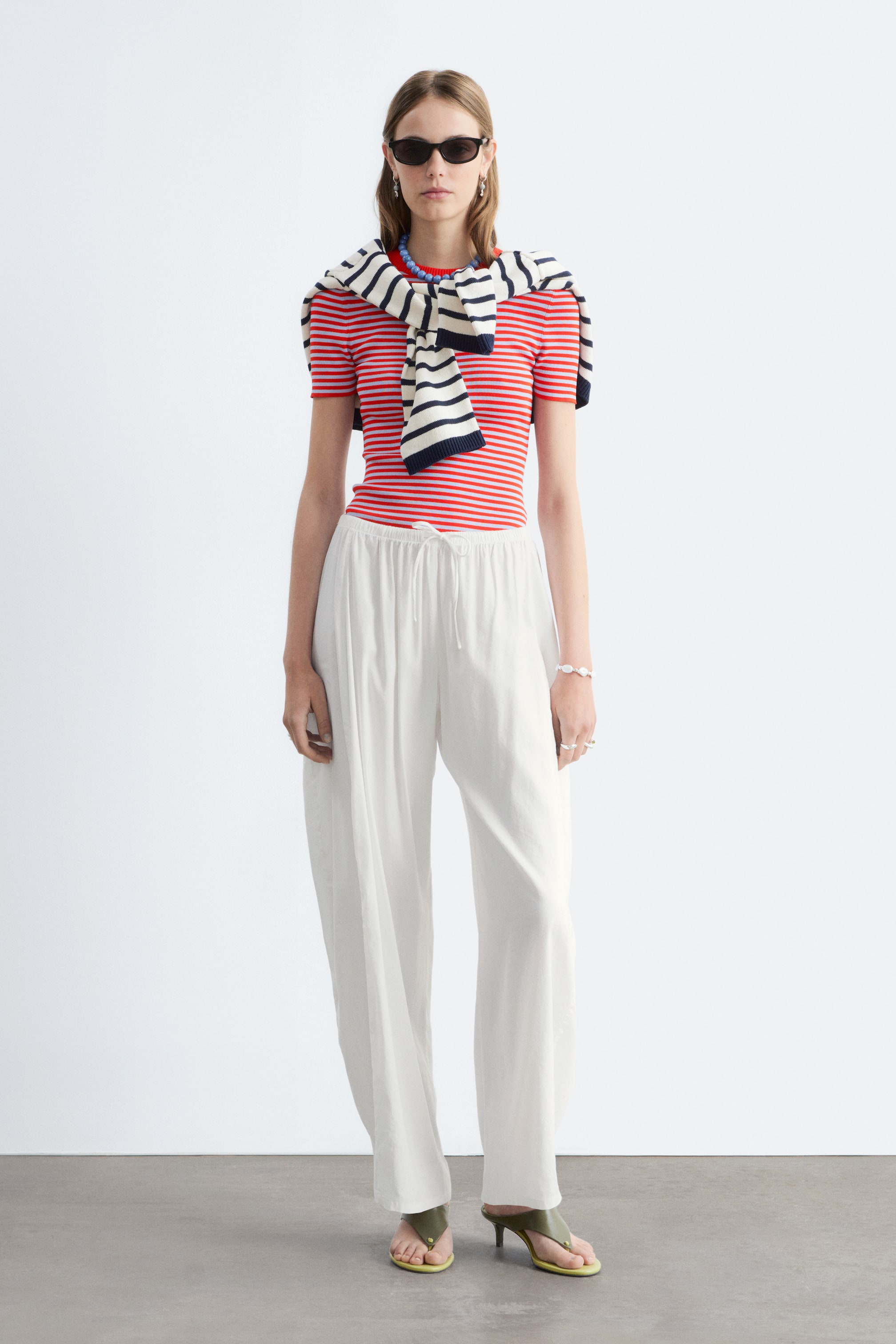 Agrandir l'image: Pantalon large blanc doté d'une taille élastiquée avec cordon de serrage. Le pantalon présente une coupe décontractée avec de subtiles plis verticaux, s'étendant jusqu'aux chevilles.