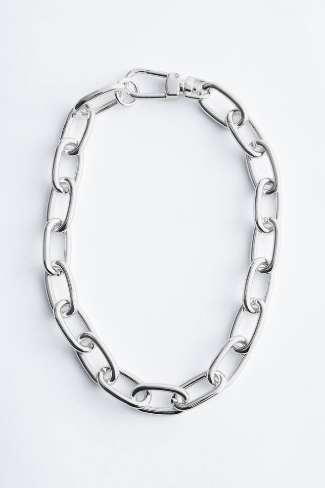 Un collier à maillons épais de couleur argentée est présenté de FACE, avec de grands maillons ovales. Un fermoir mousqueton est visible à une extrémité, formant une boucle continue. - 1