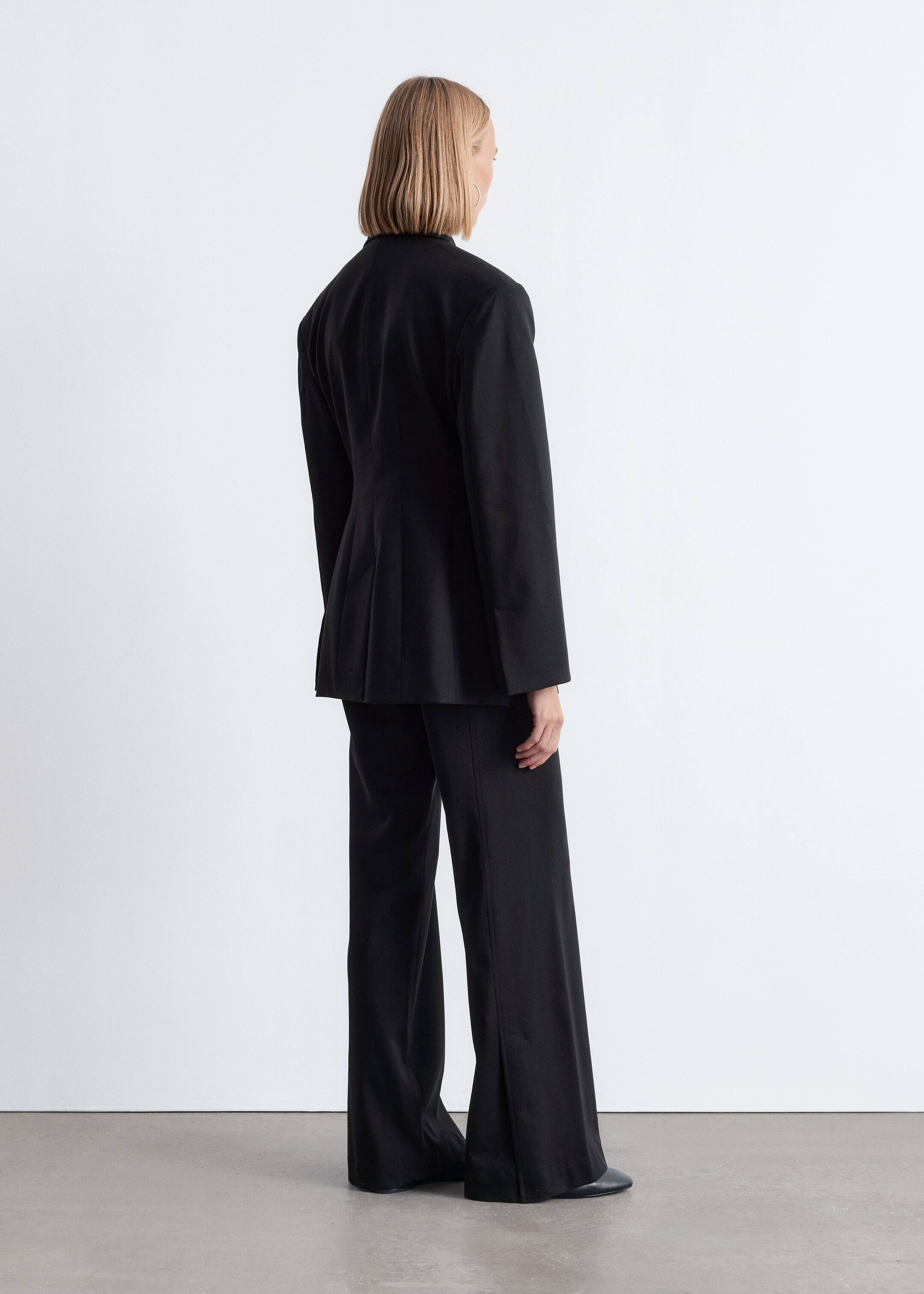 Agrandir l'image: Un tailleur-pantalon noir est présenté de dos. Le blazer ajusté présente un col haut à l'arrière et des coutures verticales, et le pantalon à jambes larges tombe jusqu'au sol.