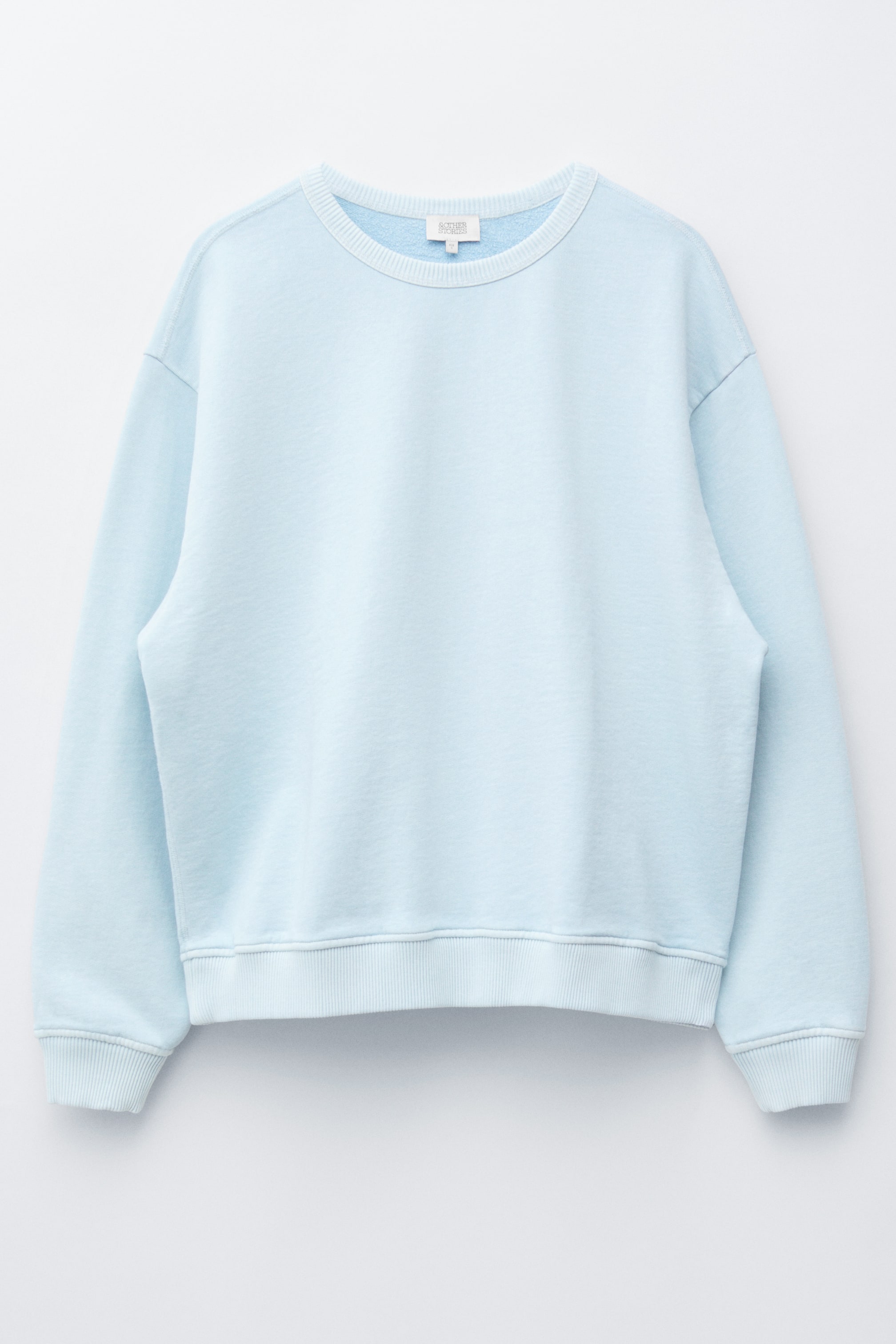 Se større billede: En lyseblå oversized sweatshirt præsenteres forfra, med en klassisk rund halsudskæring, sænkede skuldre og ribbede kanter ved halsudskæringen, manchetterne og kanten.