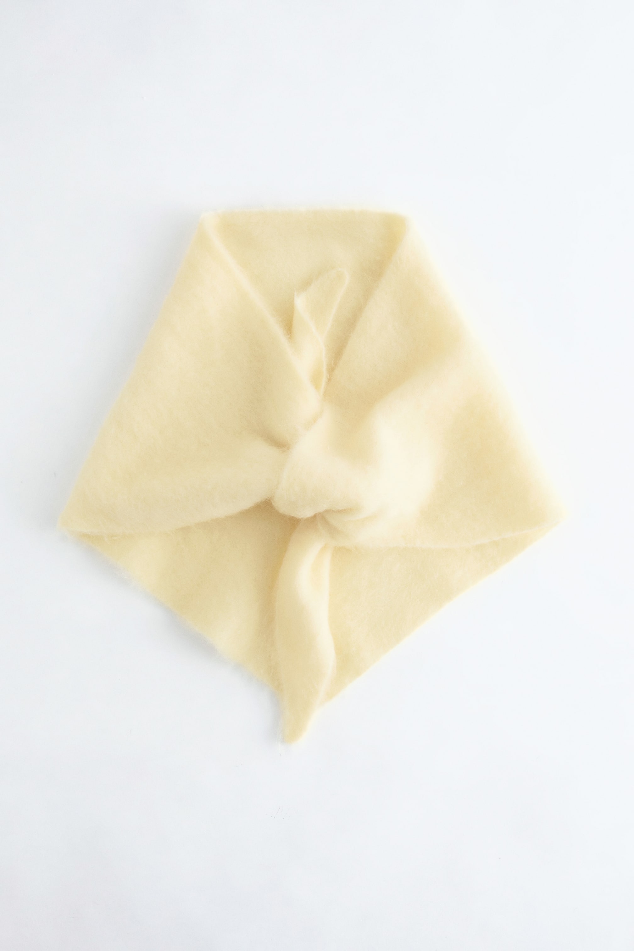 Näytä suurempi kuva: Vaaleankeltainen, pehmeä kangasneliö esitetään, taitettuna timantin muotoon ja keskellä on solmu.