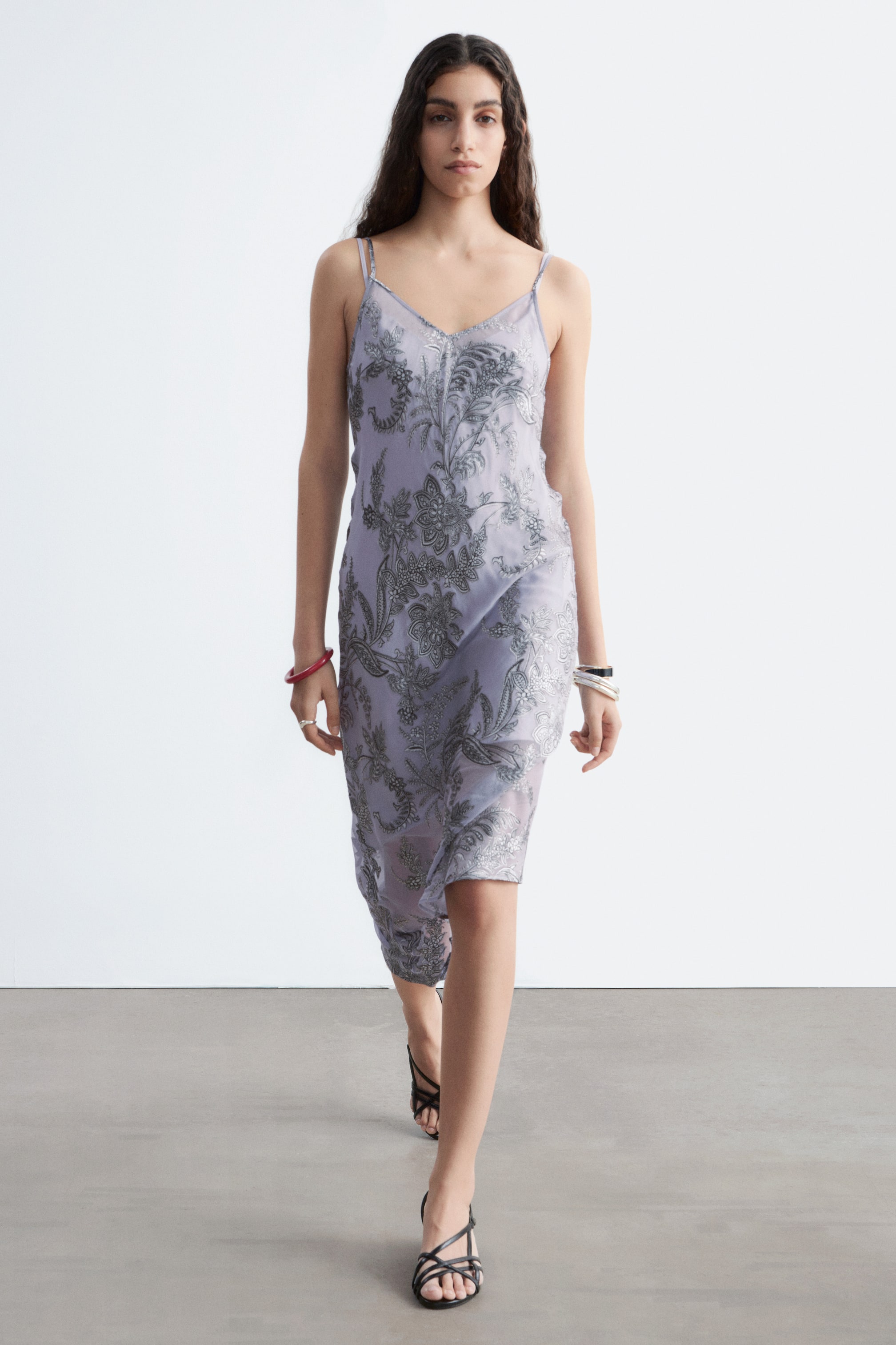 Προβολή μεγαλύτερης εικόνας: Ένα φόρεμα σε στυλ slip σε απόχρωση λεβάντας διαθέτει διαφανές επικάλυμμα με περίτεχνα ασημένια κεντήματα σε λουλούδια και παϊζλί, V-λαιμόκοψη και λεπτές τιράντες σπαγγέτι, παρουσιάζοντας μια μπροστινή όψη.