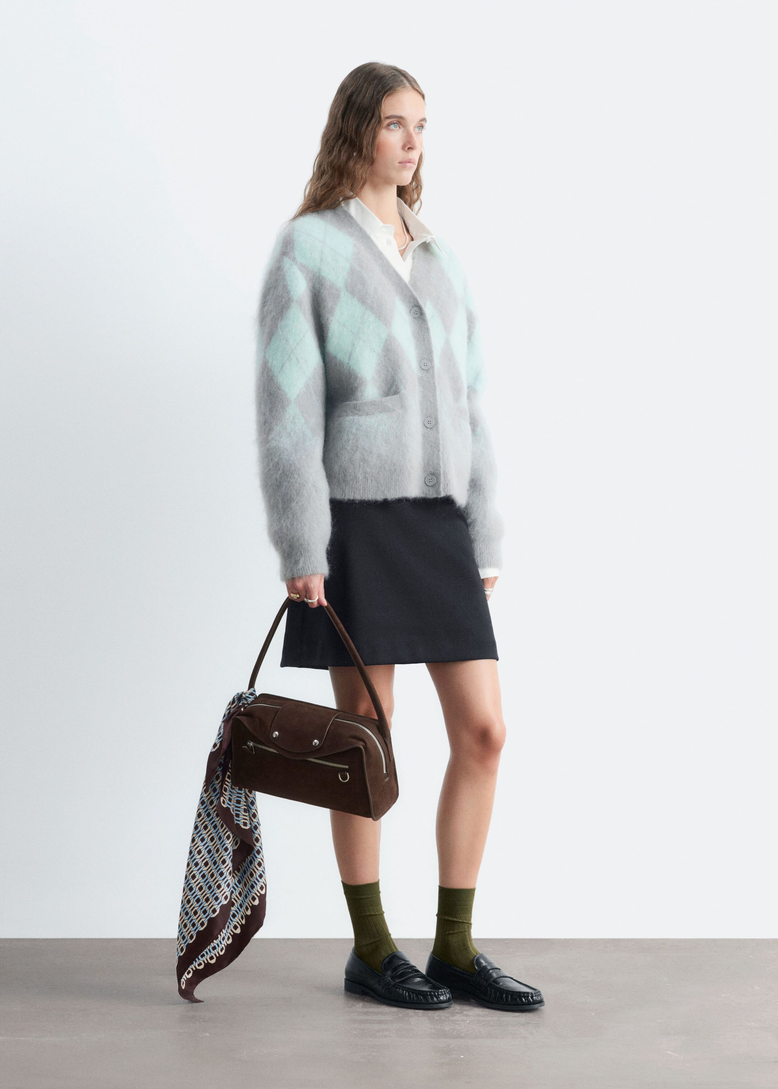 The model is wearing a mohair-blend argyle cardigan in gray and mint green over a white collared shirt and a black skirt. The cardigan features a fuzzy texture, front button closures, and patch pockets.