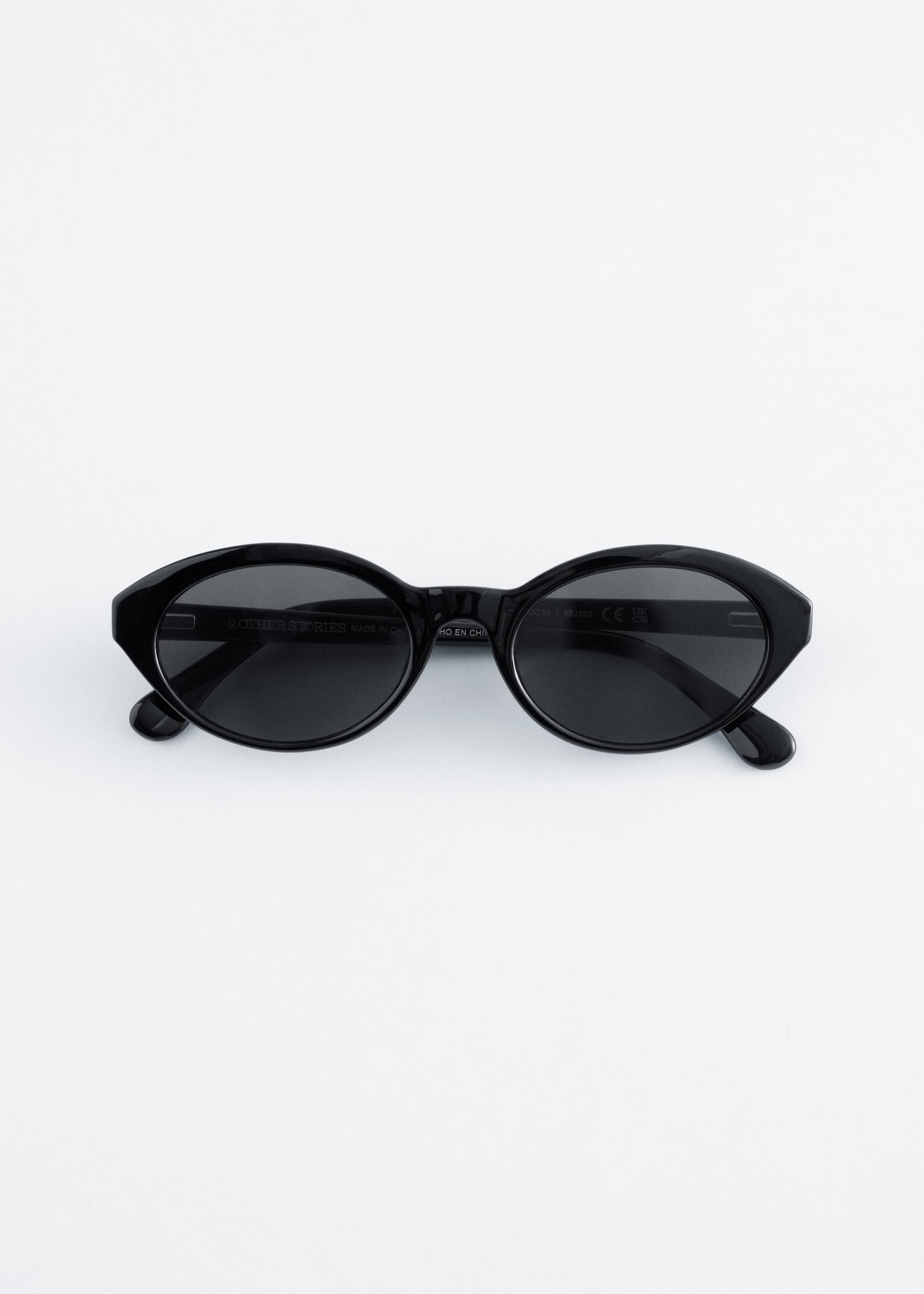 View larger image: The black sunglasses are showcased in a front view, featuring petite oval-shaped frames with a glossy finish. Shaded lenses are fitted into the frames, and slim temples extend from the sides.