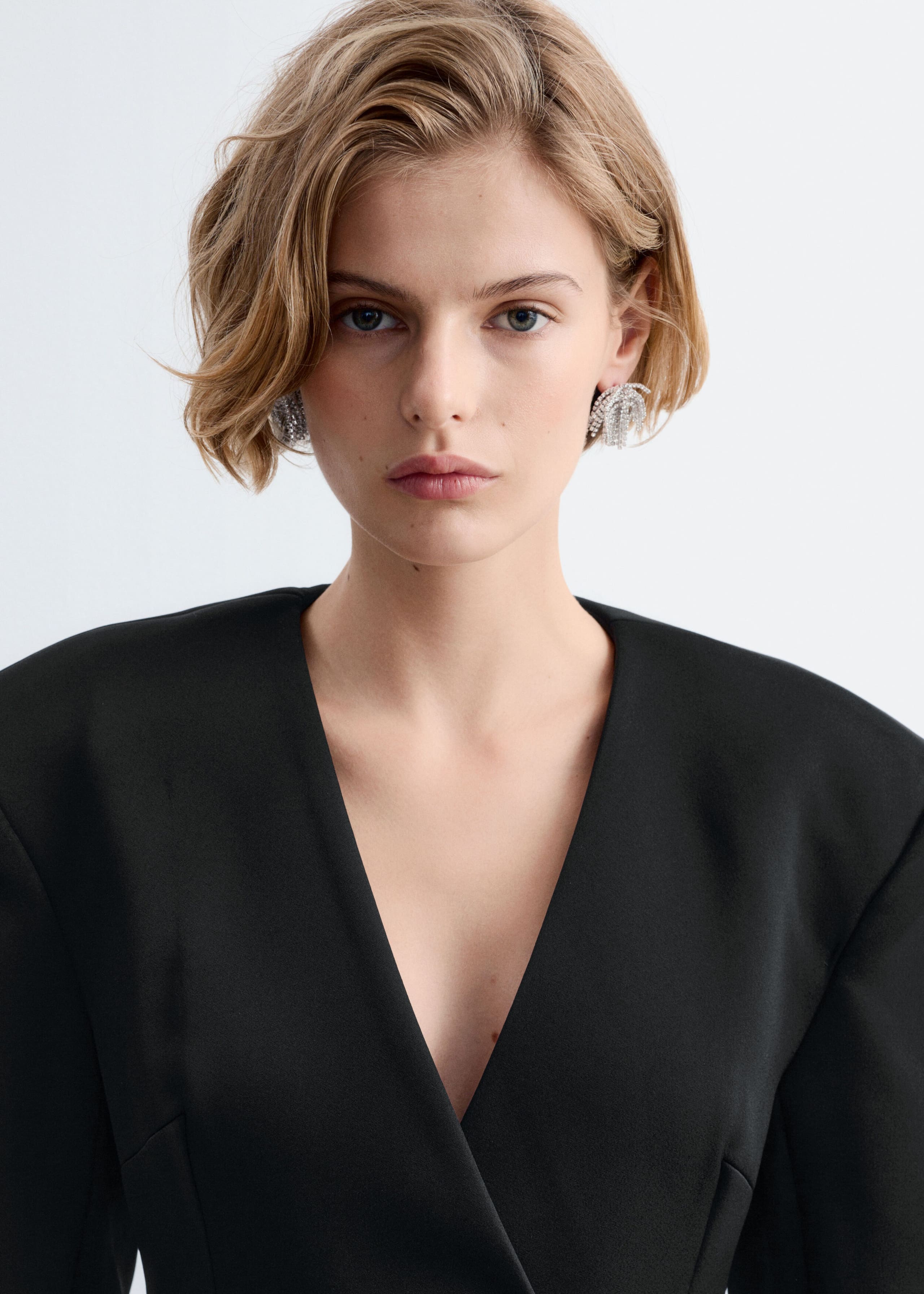 A black blazer dress with structured, padded shoulders and a deep V-neckline is being worn by the model.