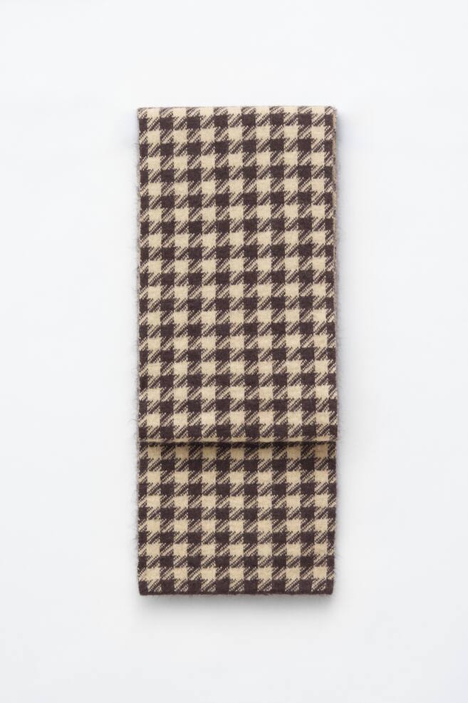A mohair-blend houndstooth scarf in dark brown and beige is lying flat and folded once horizontally, showcasing its fuzzy texture and classic pattern from a front view. - 1