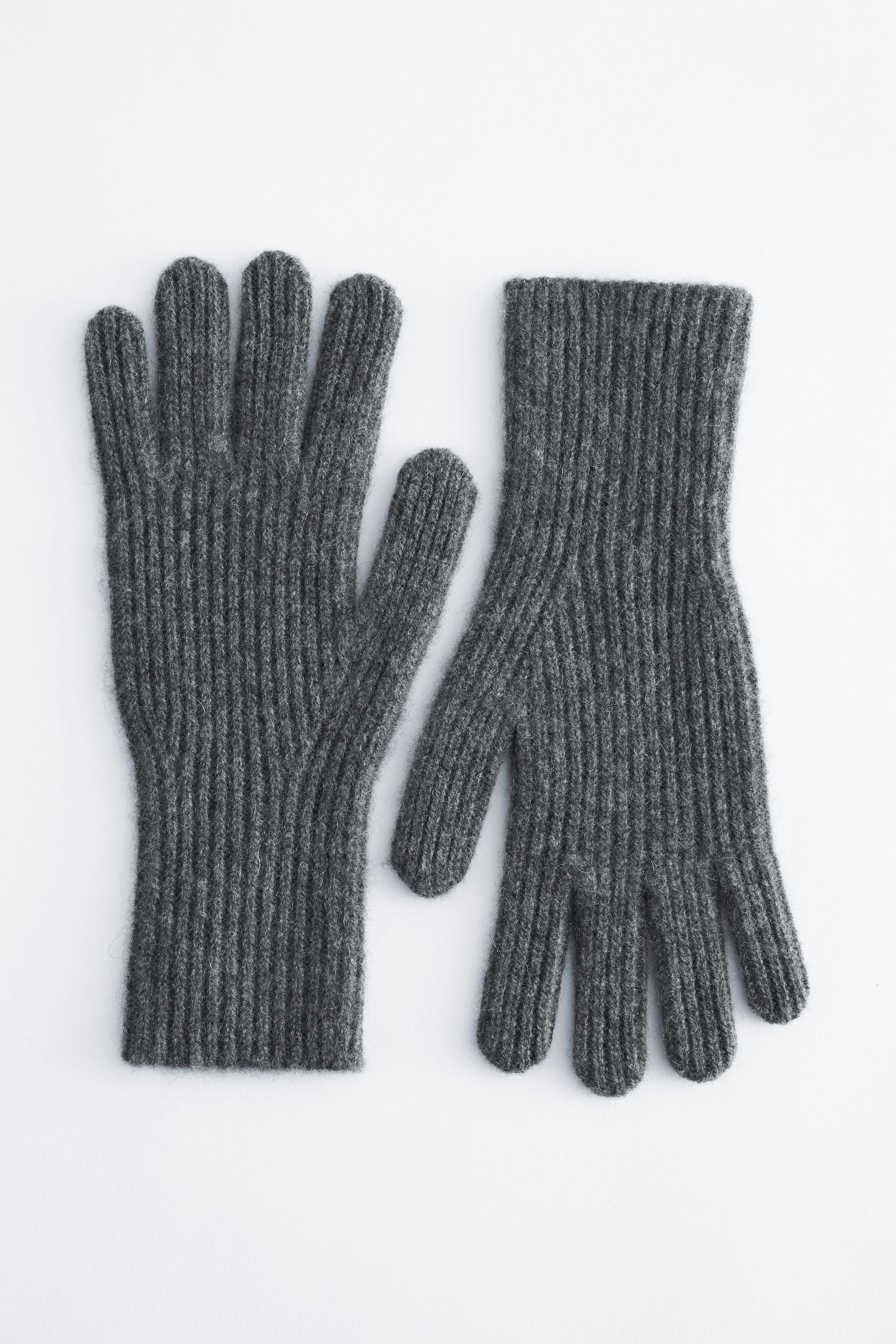Größeres Bild anzeigen: Ein Paar dunkelgraue Strickhandschuhe liegt flach und zeigt die Vorderseite mit einem sauberen Rippmuster, das die Finger, den Daumen und die Bündchen am Handgelenk bedeckt.