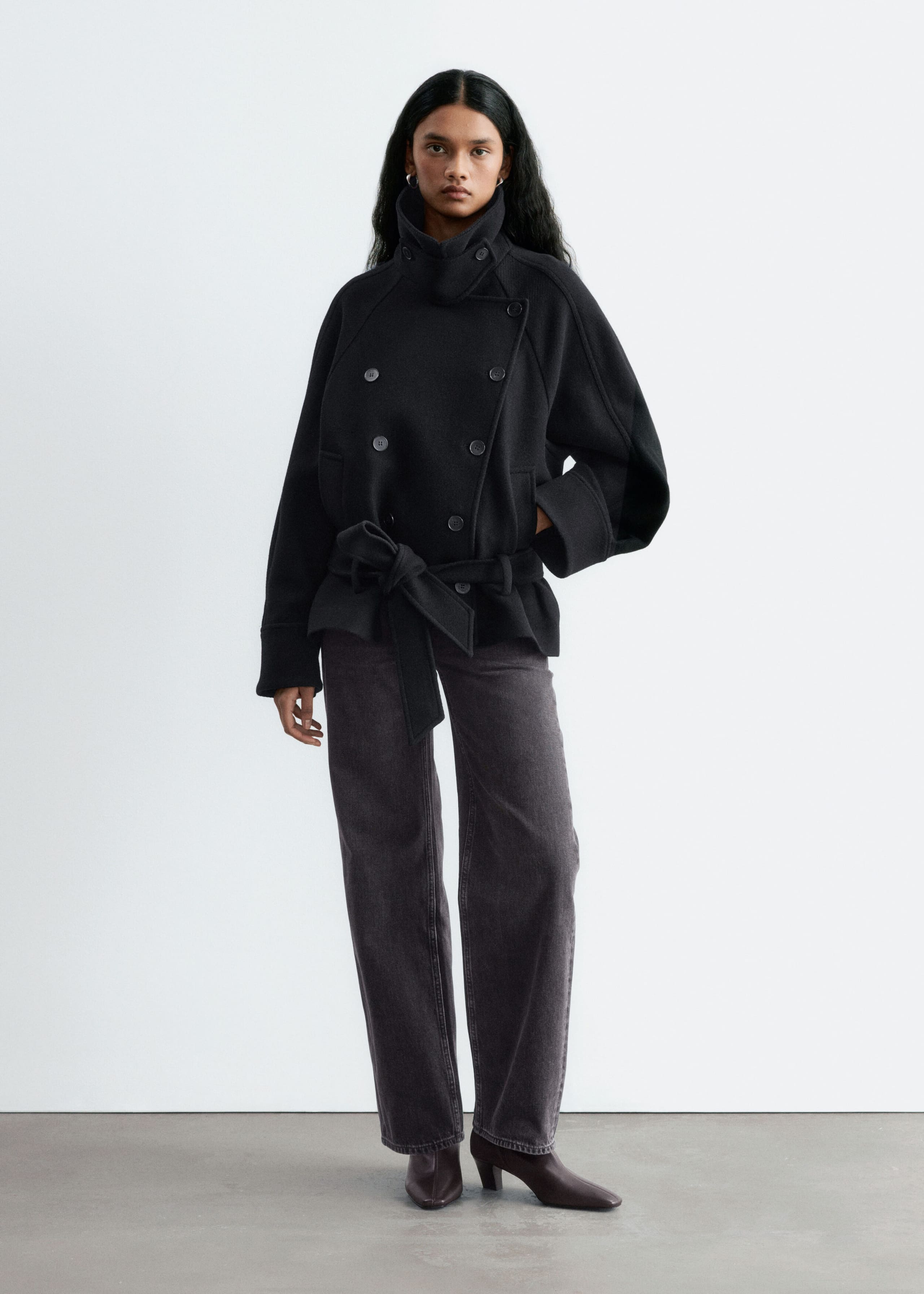 Stivaletti in pelle marrone scuro con punta quadrata, cucitura centrale frontale e tacco a blocco curvo, indossati dalla modella. Gli stivaletti sono abbinati a jeans wide-leg in denim scuro e a una giacca nera con cintura.