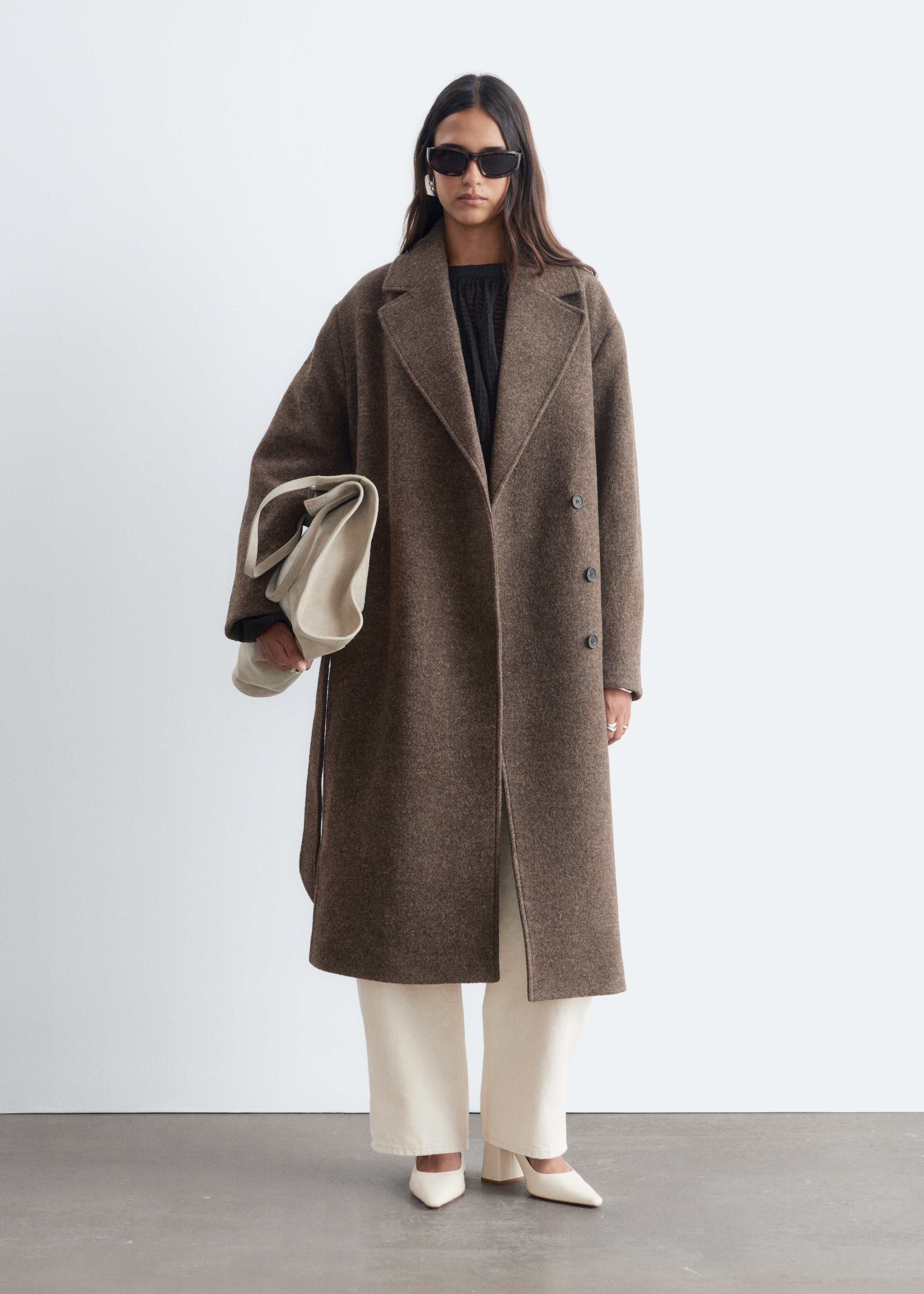 Un voluminoso cappotto di lana marrone è presentato in vista FRONTALE, caratterizzato da un revers sovrapposto e una cintura tono su tono che stringe la vita e annodata in un nodo.