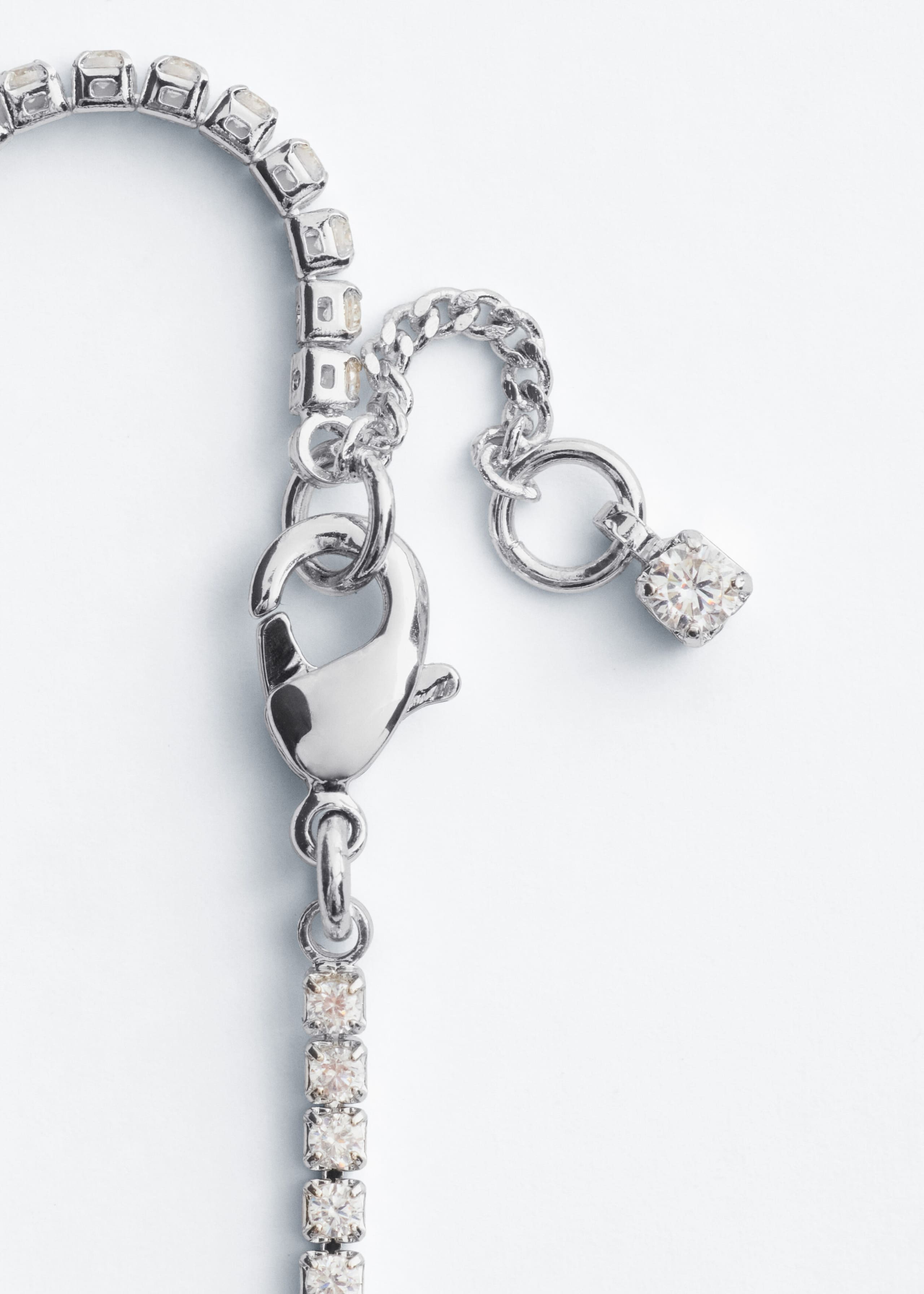 A silver-toned brass bracelet set with square-cut rhinestones is shown displaying its fastening mechanism, featuring a lobster clasp and an adjustable extension chain. The extension chain ends with a single square-cut rhinestone charm.