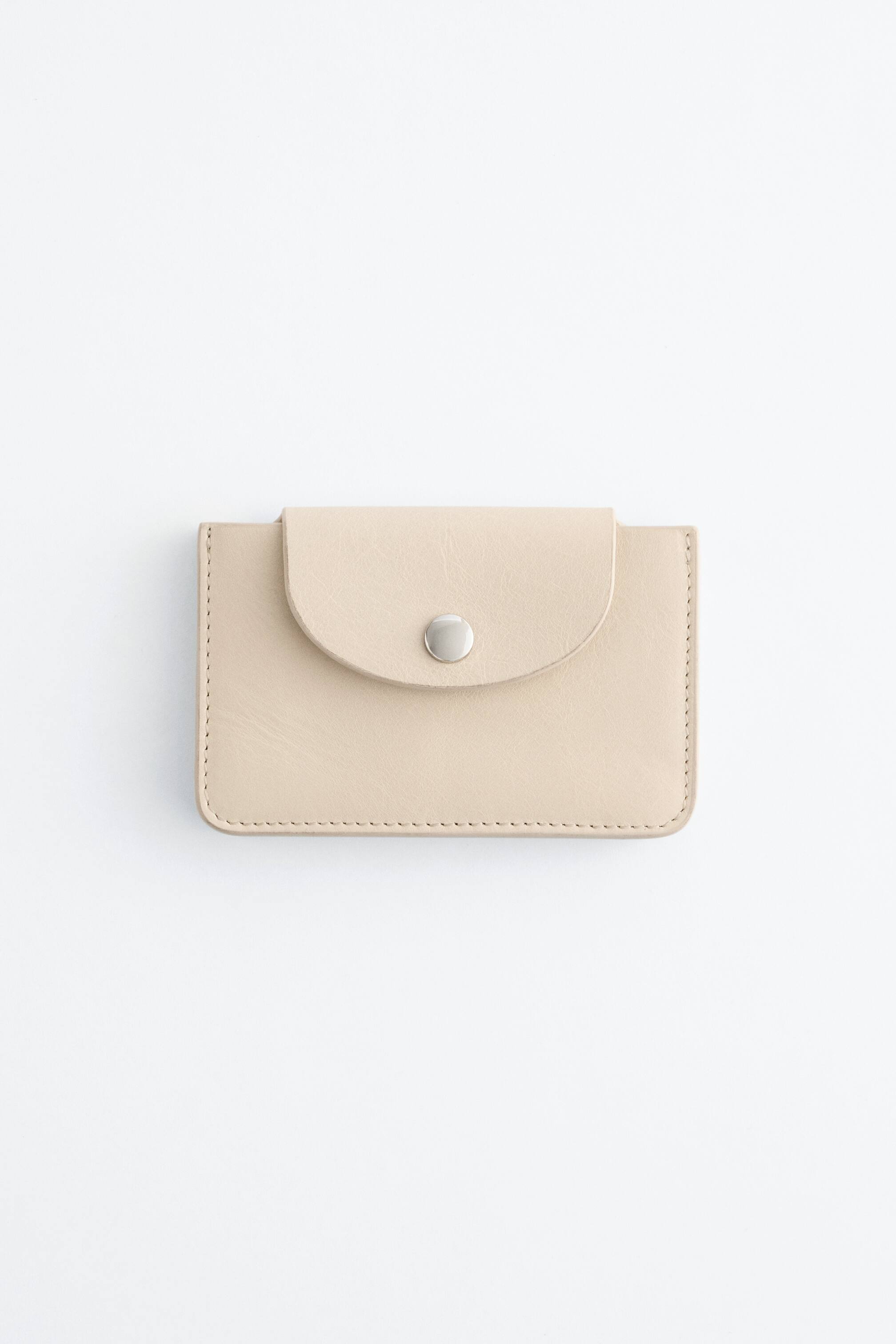 Преглед на по-голямо изображение: Светло бежов държач за карти е представен в преден изглед, с извит капак и сребристо-затворен с натиск бутон. Видими шевове подчертават краищата му.