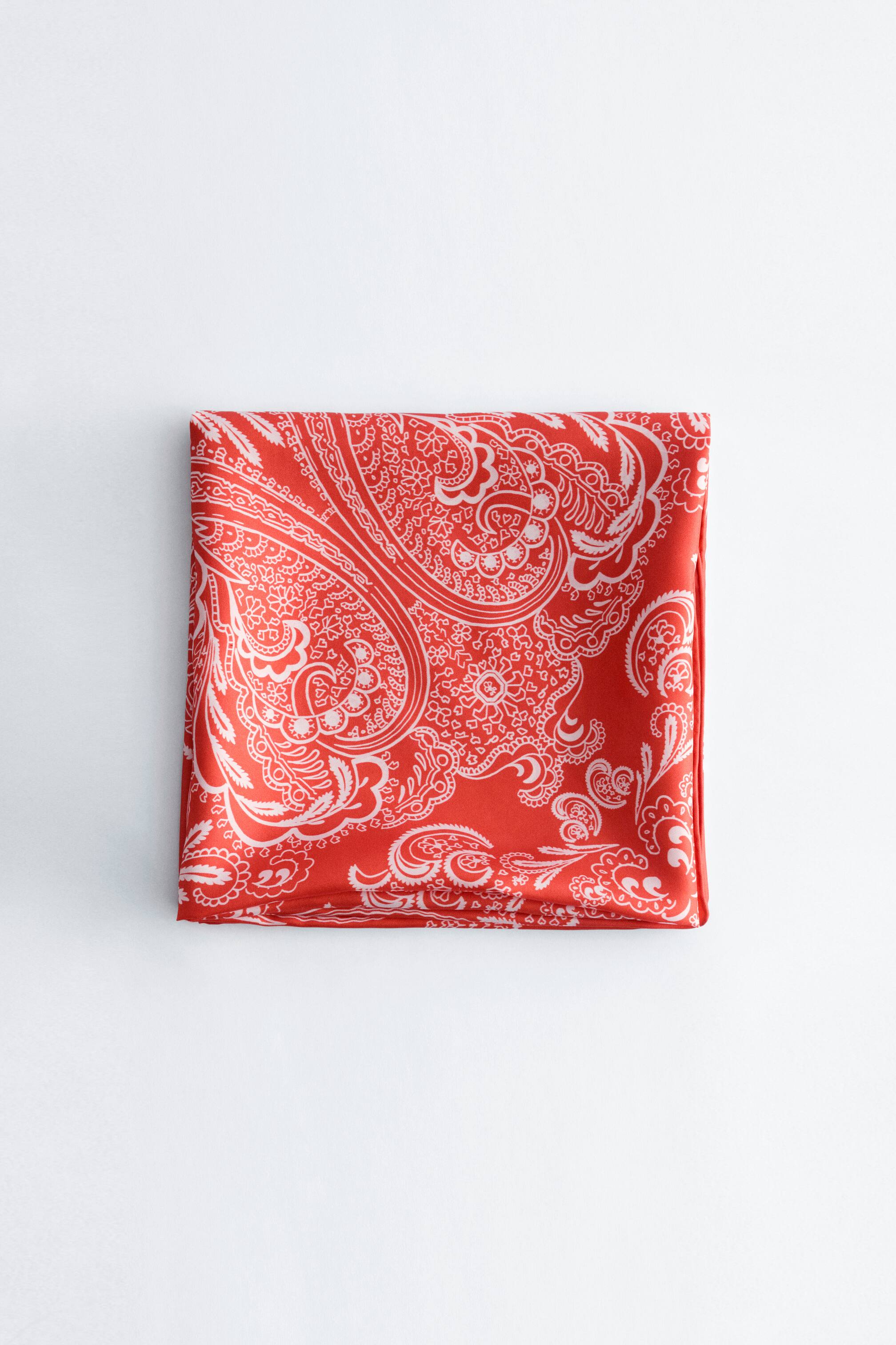 Se større billede: Paisley silketørklæde med et hvidt paisleymønster på en rød baggrund, pænt foldet i en firkant.