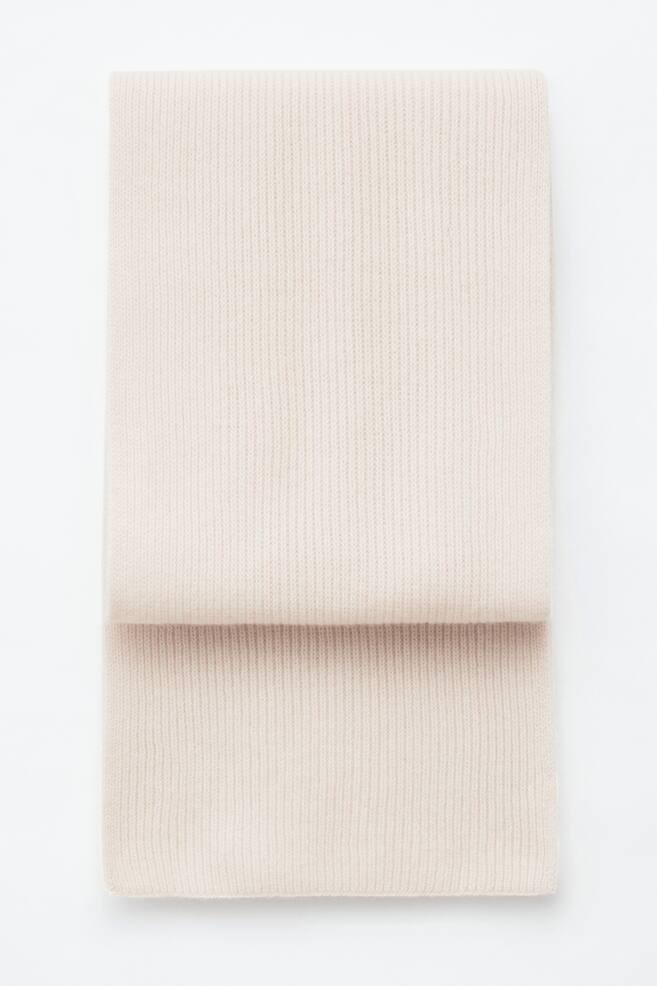 Ein hellcremefarbener Kaschmir-Strickschal mit vertikal gerippter Struktur liegt flach gefaltet da und prÃ¤sentiert seine weiche Textur sowie saubere, gerade Kanten. - 1
