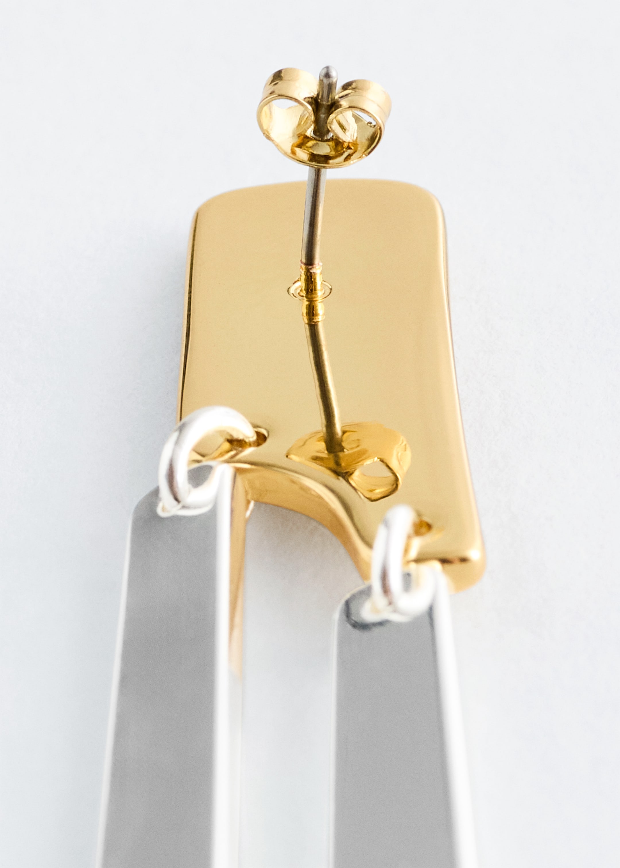 View larger image: The BACK of a two-tone pendant earring is being shown, featuring interlinked plates. The polished gold-tone rectangular top plate is presenting a post and butterfly backing, while two polished silver-tone rectangular plates are hanging below it.
