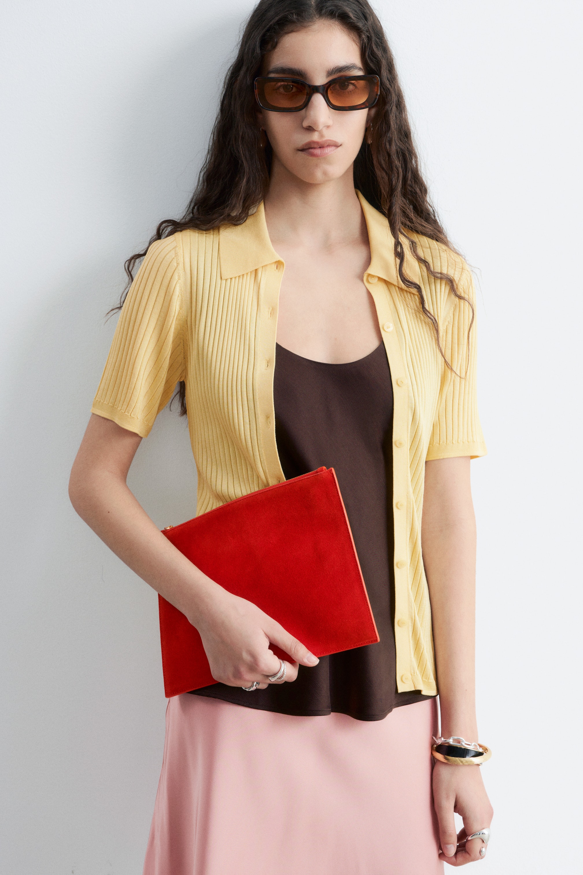 Agrandir l'image: Une pochette plate rectangulaire en daim rouge avec une fermeture éclair visible le long de son sommet est tenue par le mannequin.