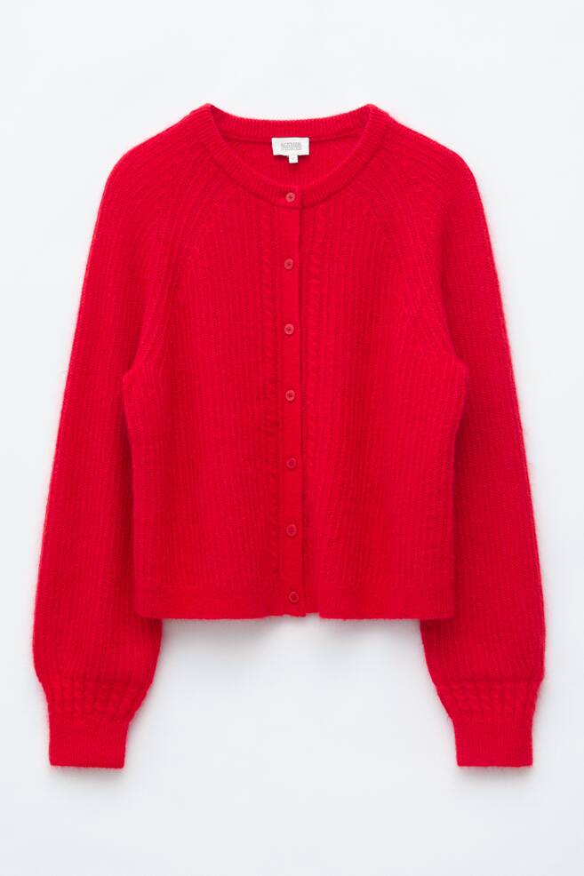 A front-facing view of a bright red mohair-blend cardigan laid flat, featuring long raglan sleeves, a crew neckline, and a buttoned front placket. The cardigan displays cable detailing running vertically along both sides of the placket and above the cuffs, finished with a ribbed texture at the neckline, cuffs, and hem. - 1