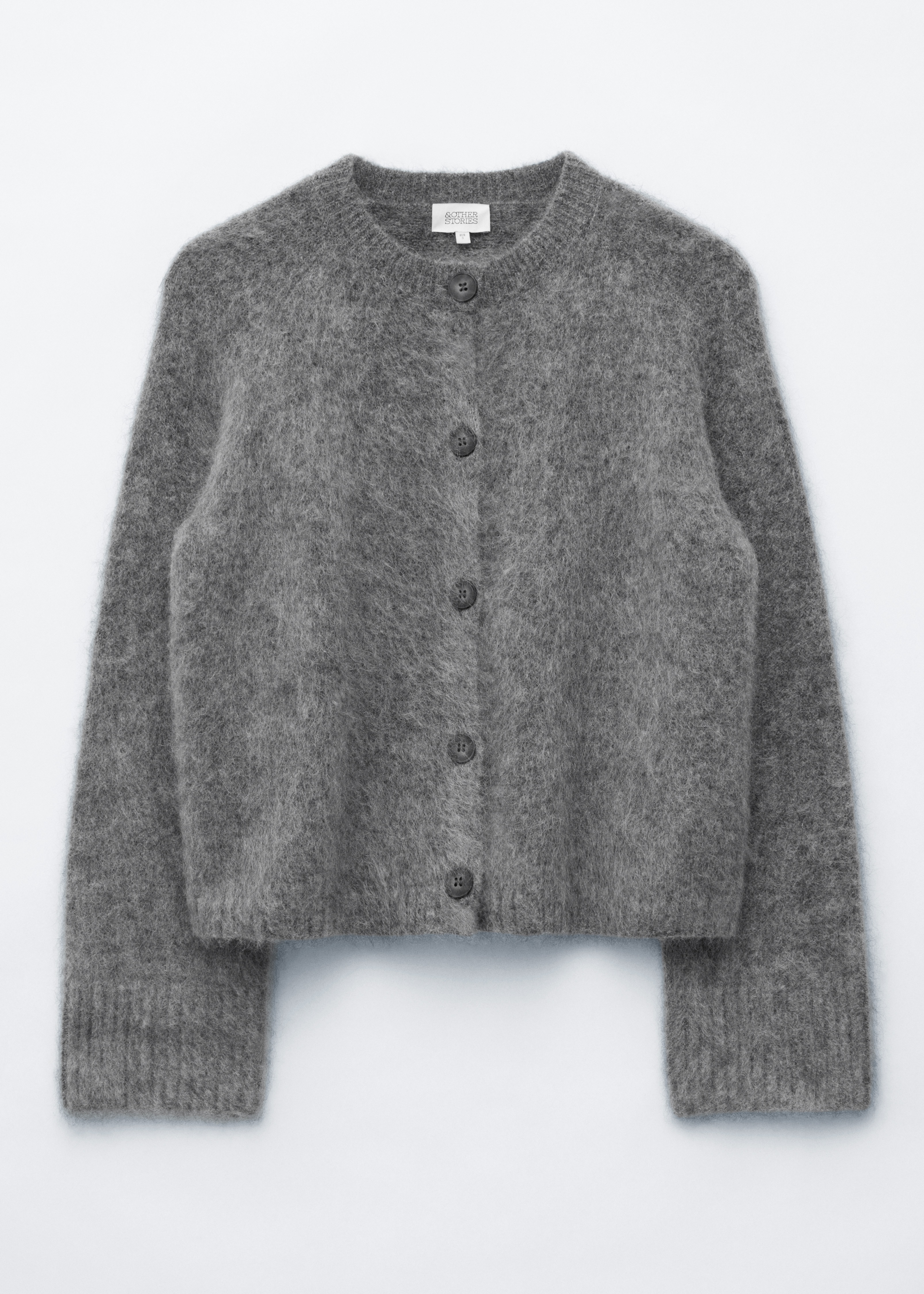 Ein grauer Strickjacken-Mohair-Mix mit flauschiger Textur, Rundhalsausschnitt und dunklen FrontknÃ¶pfen wird vom Model getragen. Die Strickjacke ist Ã¼ber einem weiÃen T-Shirt und einem karierten Rock gestylt, wÃ¤hrend das Model eine schwarze Leder-Clutch trÃ¤gt.