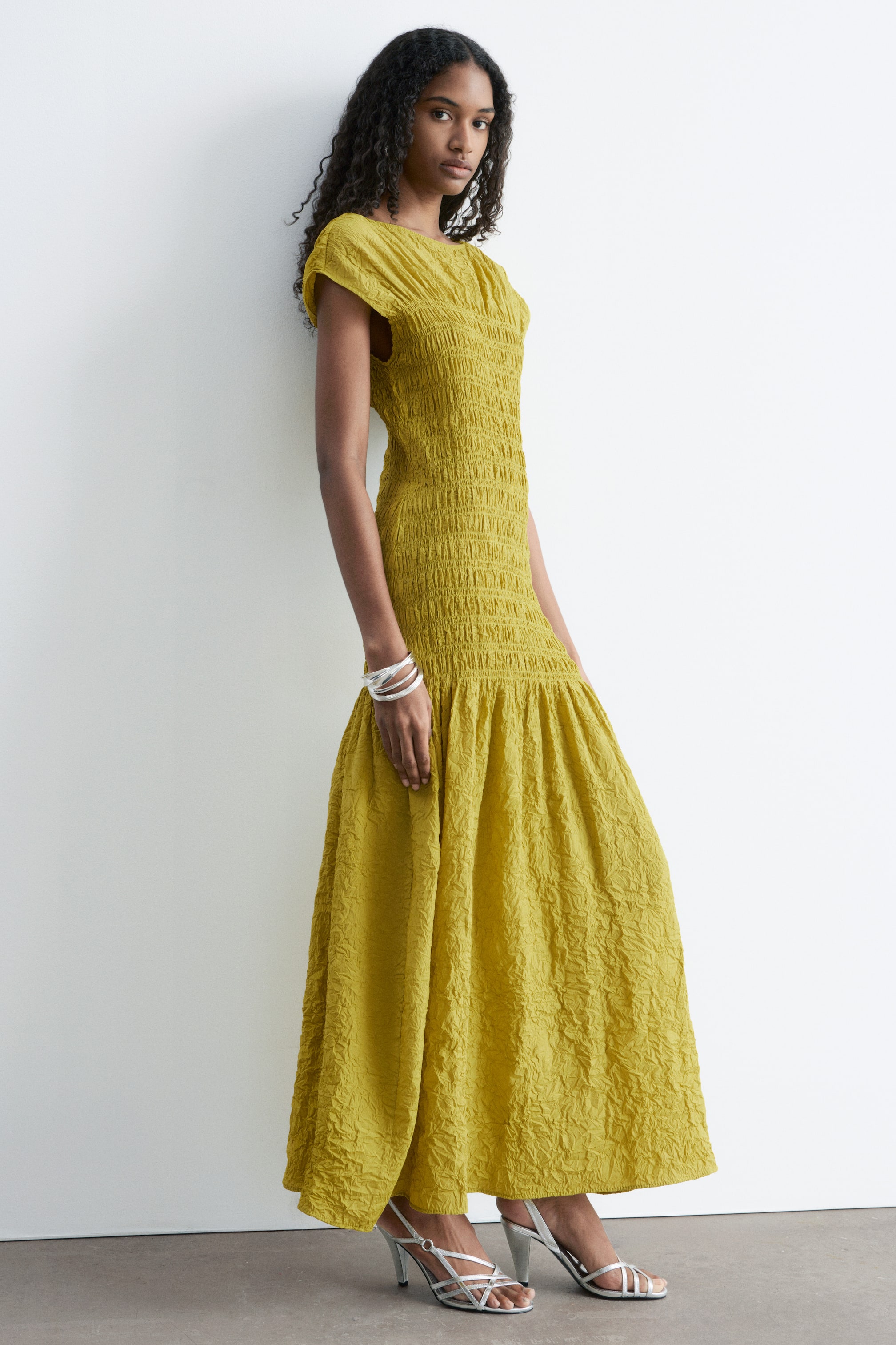 Größeres Bild ansehen: Ein chartreusefarbenes Maxikleid mit einem gerafften Oberteil, einem runden Ausschnitt und kurzen Ärmeln, das in einen vollen, geknitterten Rock übergeht.