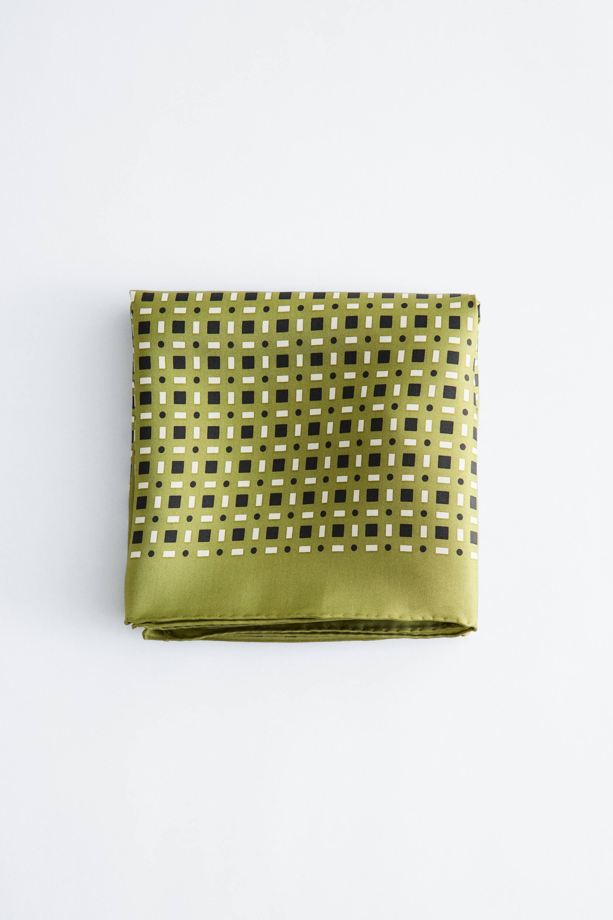 הצגת תמונה גדולה יותר: צעיף מונח מקופל לצורת מלבן, עם בסיס ירוק ליים ודגם גיאומטרי חוזר של ריבועים שחורים, ריבועים לבנים ונקודות שחורות קטנות.