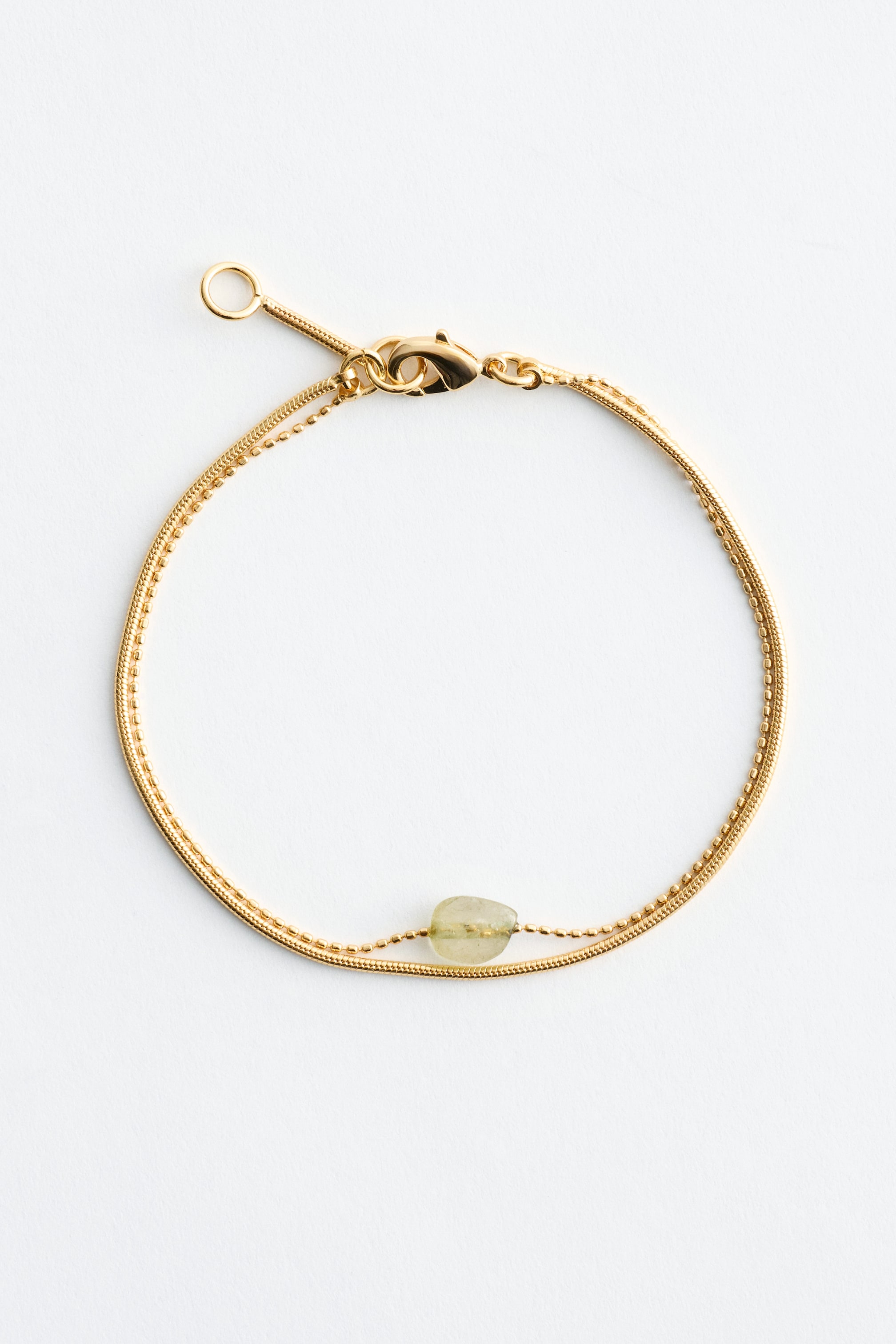 Zobraziť väčší obrázok: Dvojvrstvový náramok zobrazuje dve jemne leštené mosadzné retiazky, jednu hladkú a jednu korálkovú. Svetlozelený, nepravidelný kameň z kremeňa je navlečený na korálkovej retiazke a zapínanie na pracku zabezpečuje náramok.